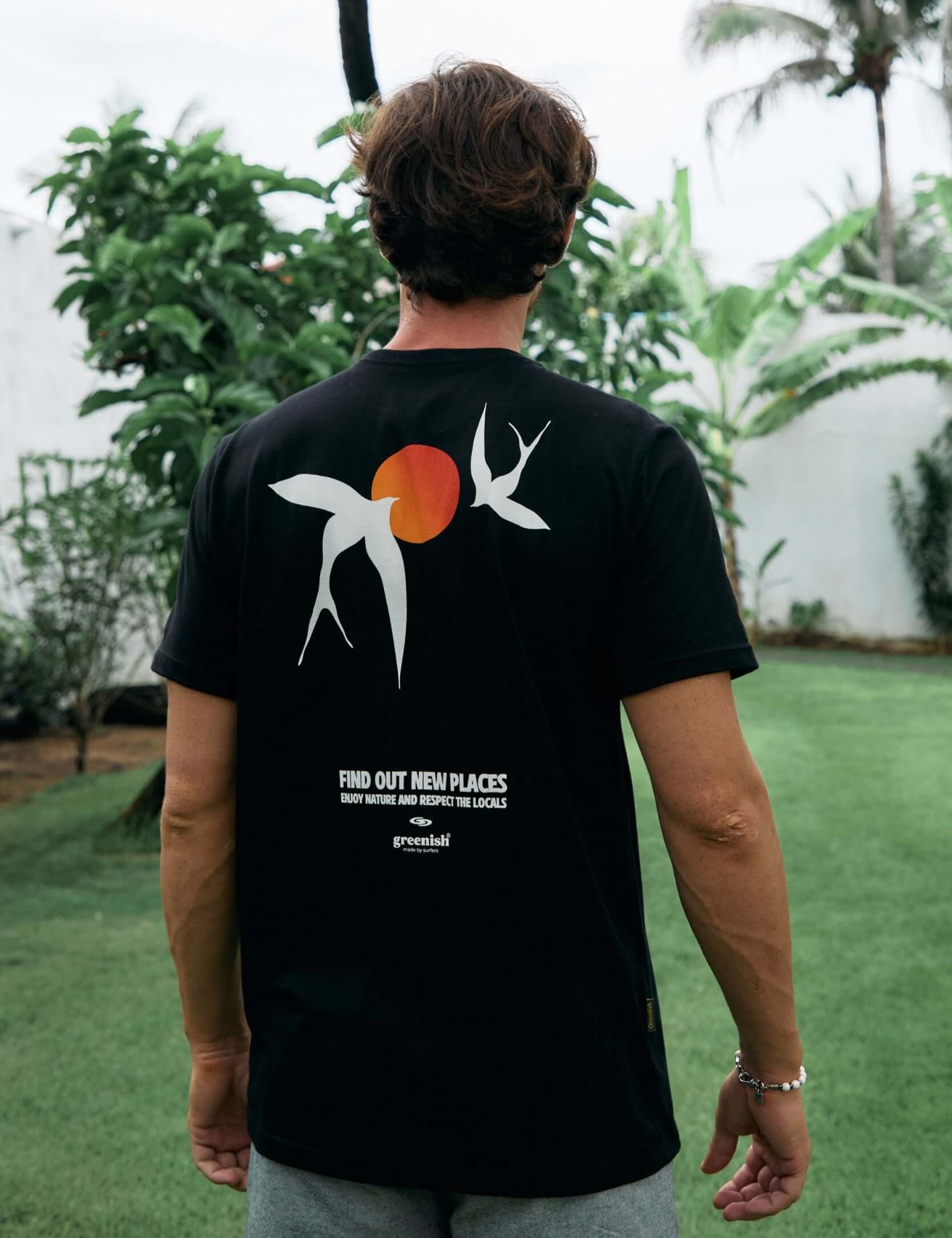 Homem usando a Camiseta Seagull preta da Greenish com arte inspirada em gaivotas e sol, em ambiente natural ao ar livre.