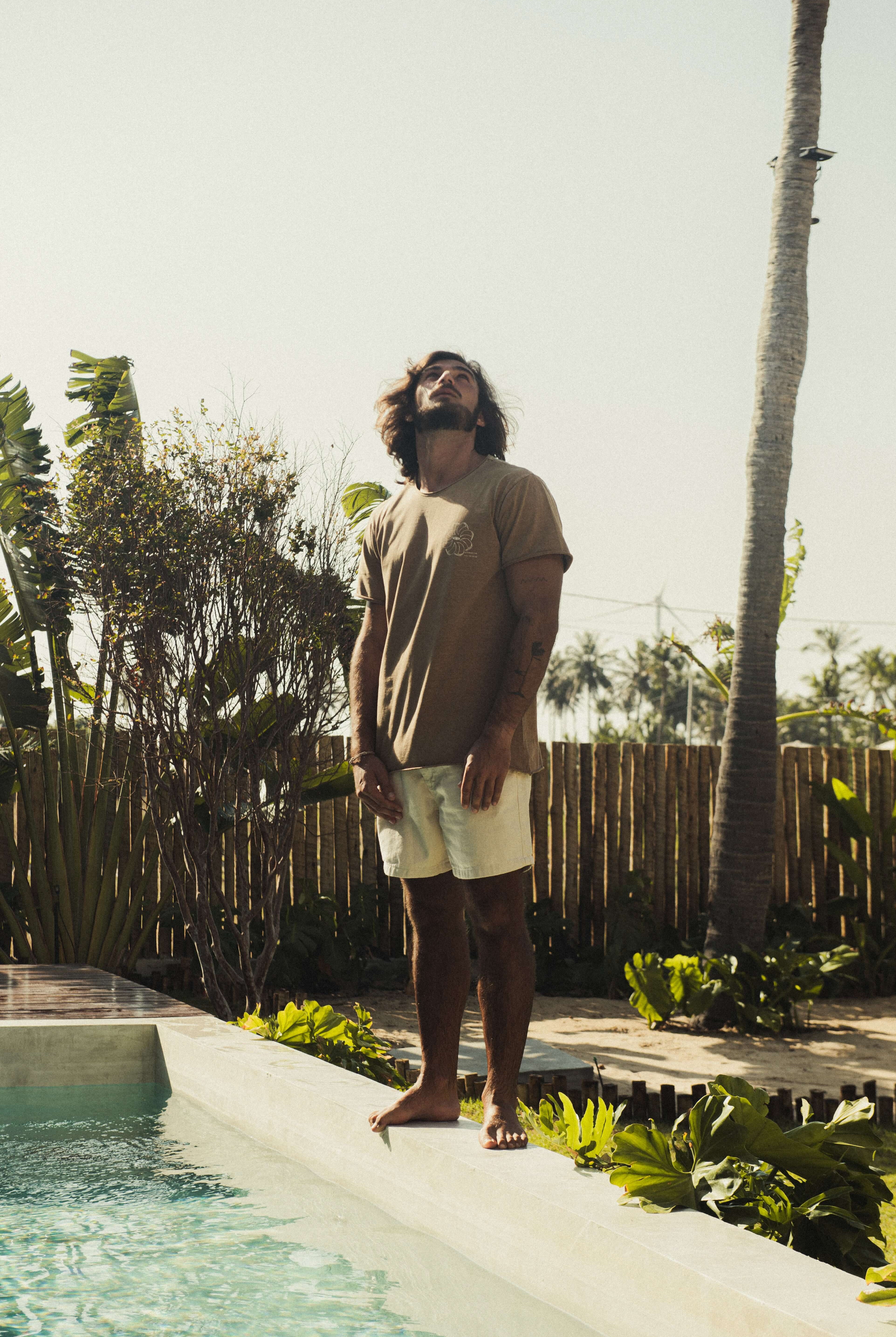 Homem ao ar livre vestindo Camiseta Stone Feel The Winds - Marrom da Greenish, com toque macio e visual rústico em um ambiente tropical.