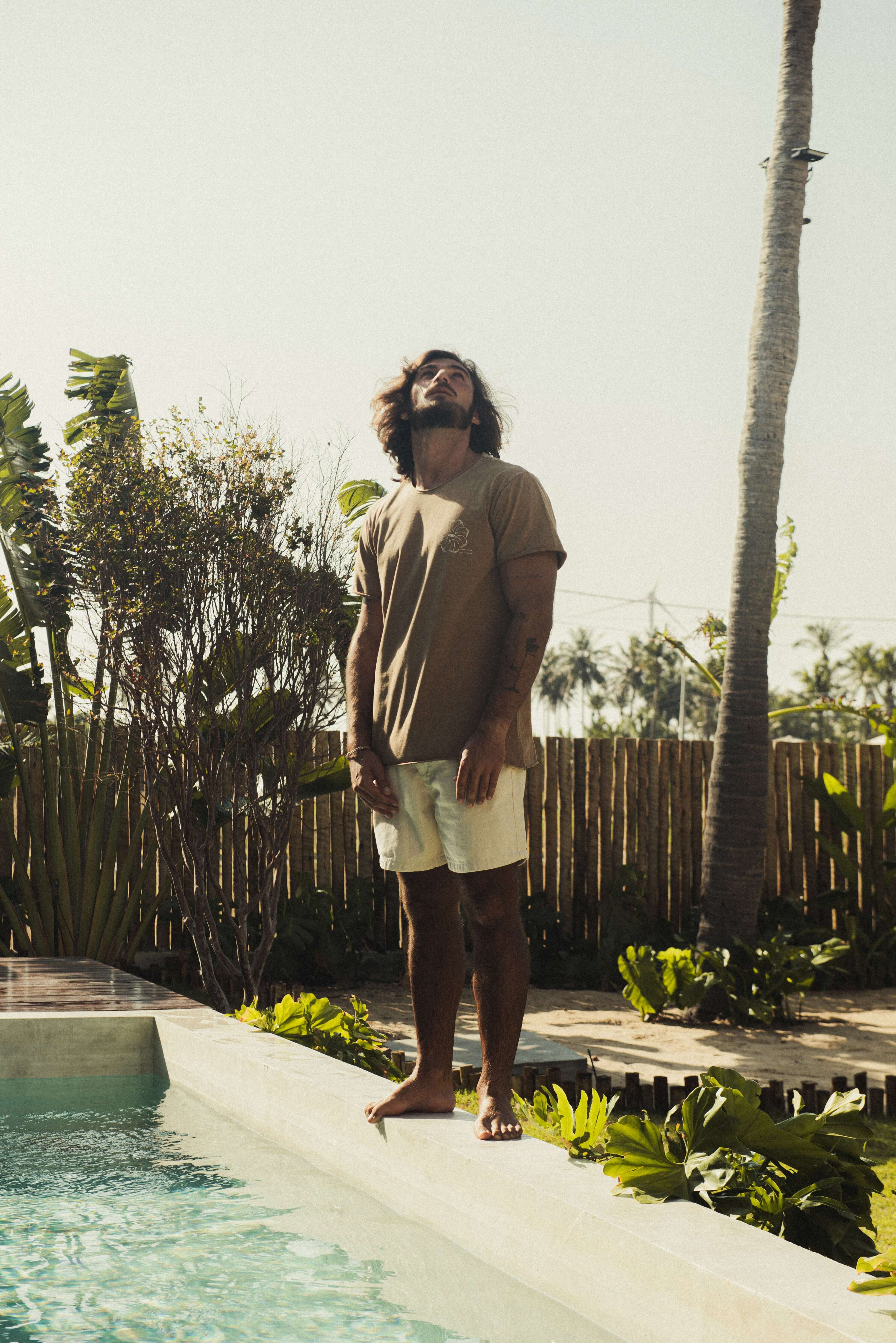 Homem ao ar livre vestindo Camiseta Stone Feel The Winds - Marrom da Greenish, com toque macio e visual rústico em um ambiente tropical.