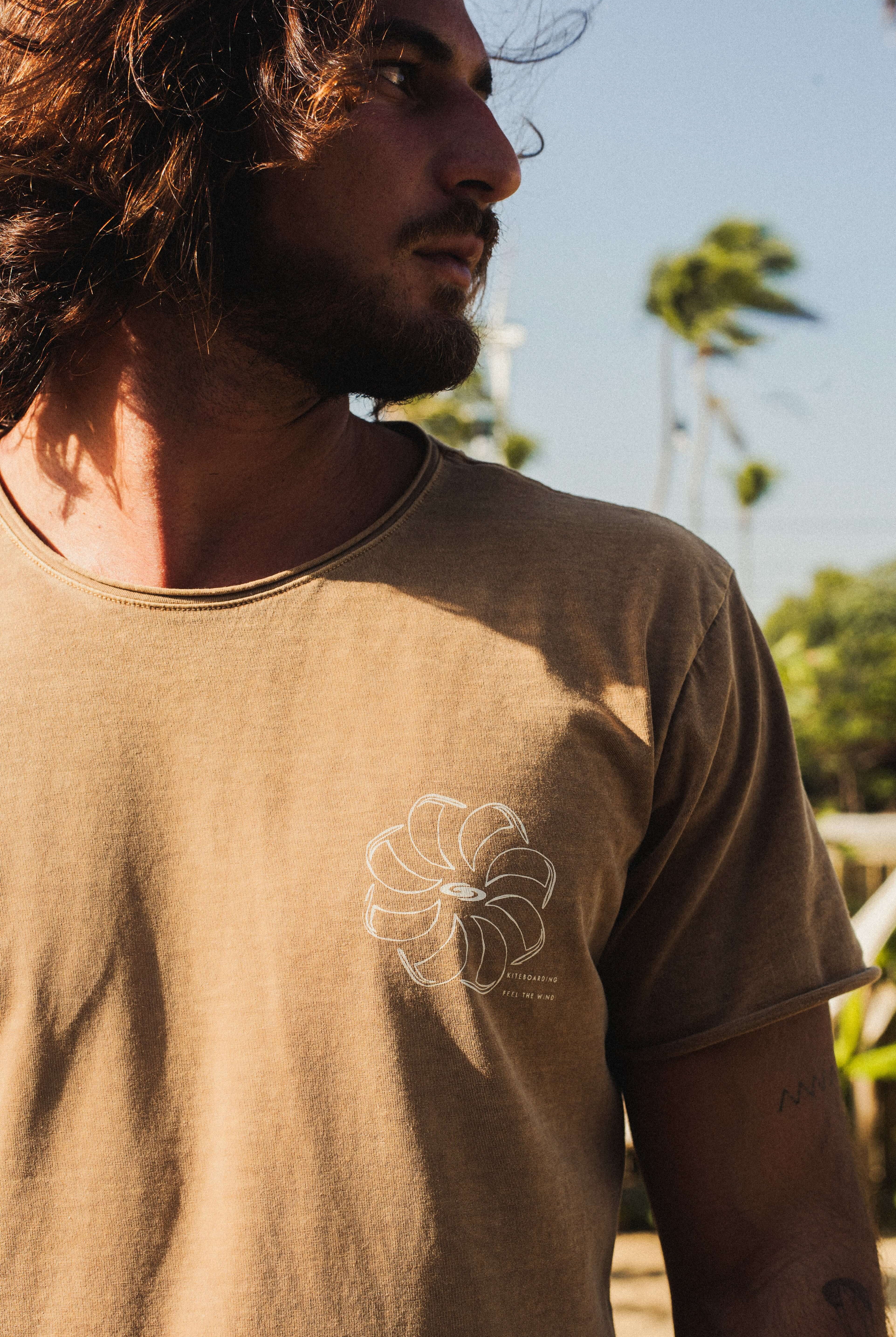 Camiseta Stone Feel The Winds - Marrom, Greenish, em algodão com visual rústico e estampada, usada por homem ao ar livre com vento.