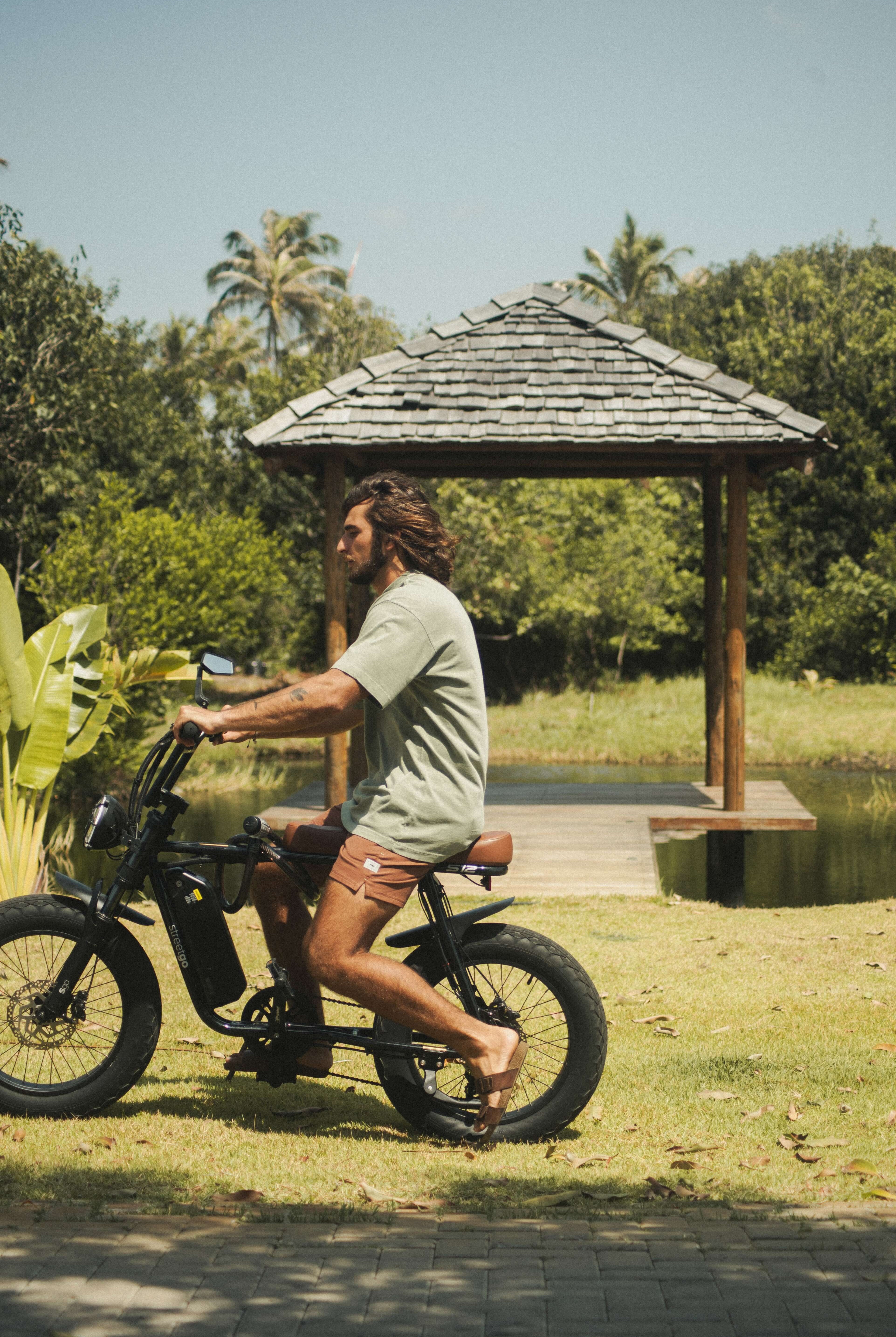 Homem usando Camiseta Stone Oversized Greenish - Verde da marca Greenish pedalando tranquilamente ao ar livre.