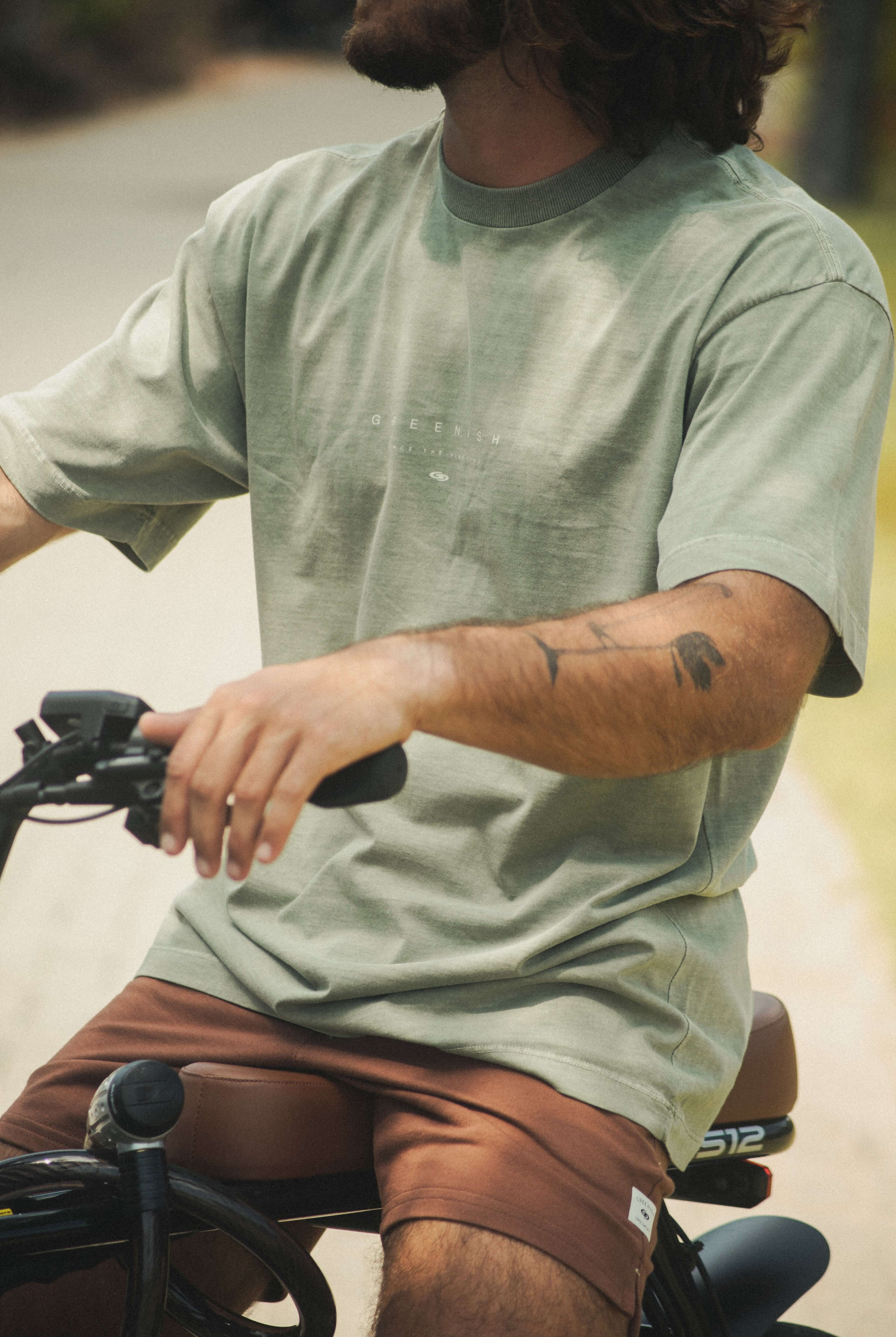 Jovem em bicicleta vestindo Camiseta Stone Oversized Greenish - Verde da Greenish, estilo vintage com caimento solto e toque aveludado.