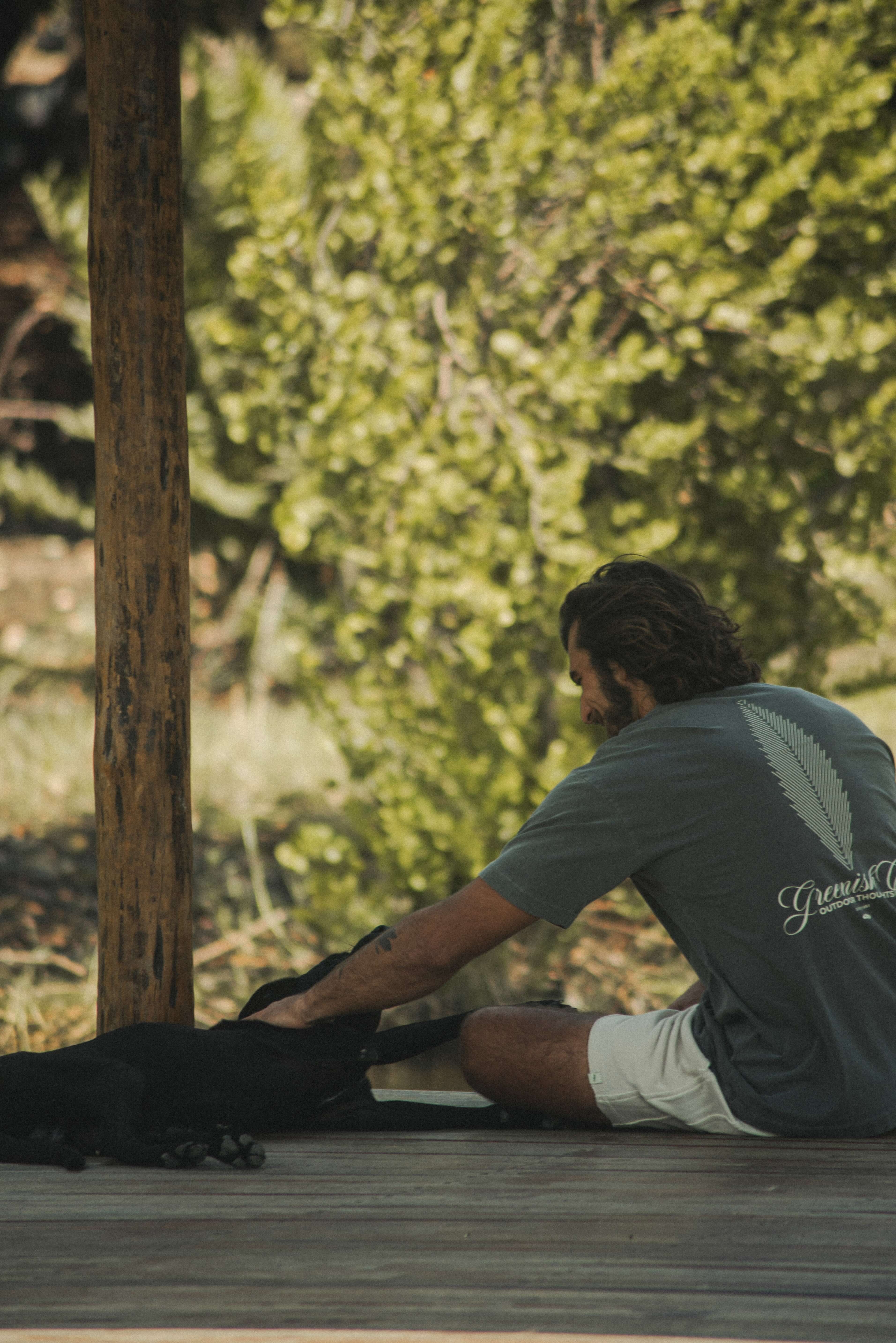 Homem usando Camiseta Oversized Stong Leaf Plank - Chumbo da Greenish, sentado em deck de madeira com cachorro, com visual vintage.