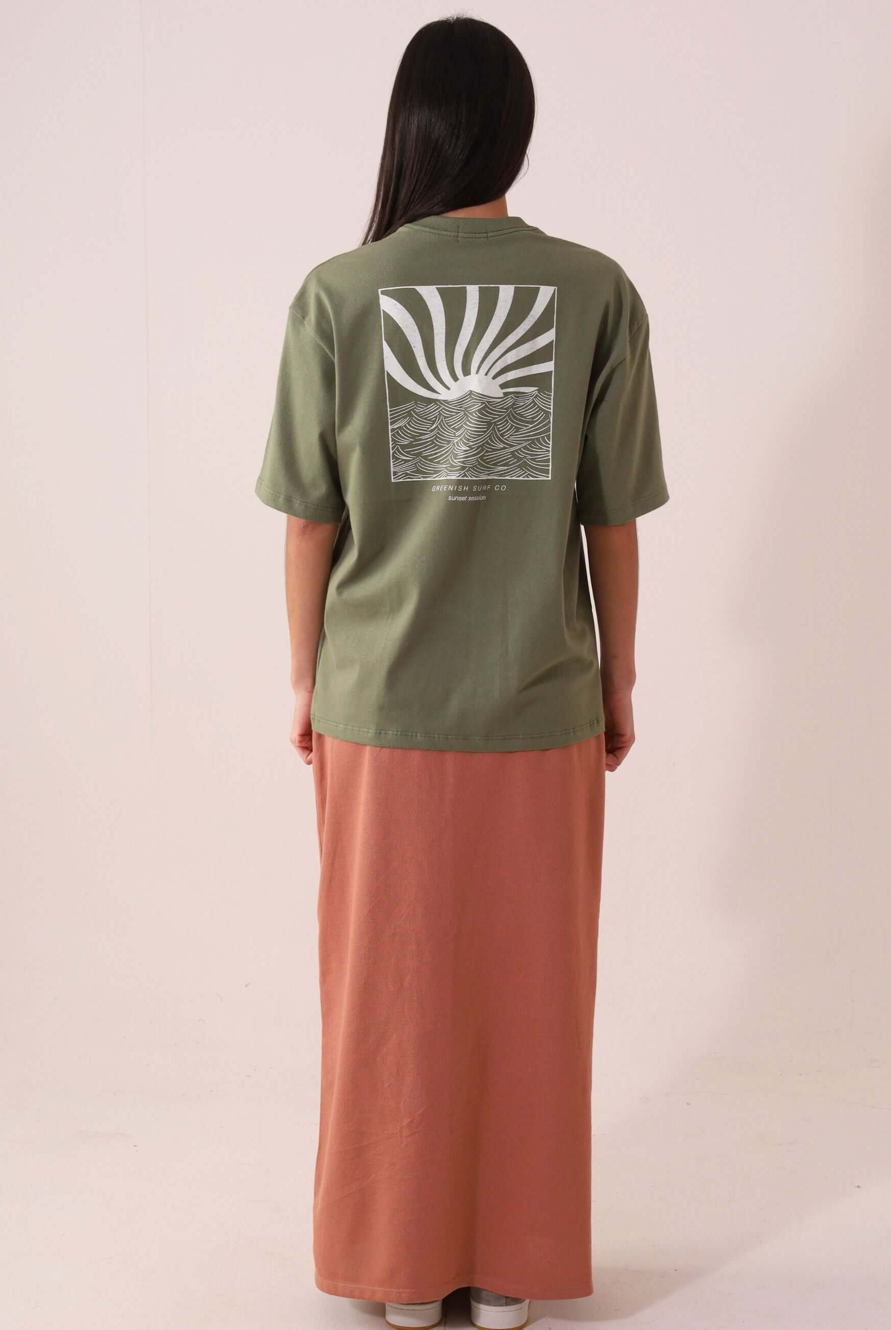 Mulher vestindo CAMISETA OVERSIZED SUNSET SESSION - VERDE Greenish com estampa de ondas e pôr do sol, vista traseira, estilo e conforto.