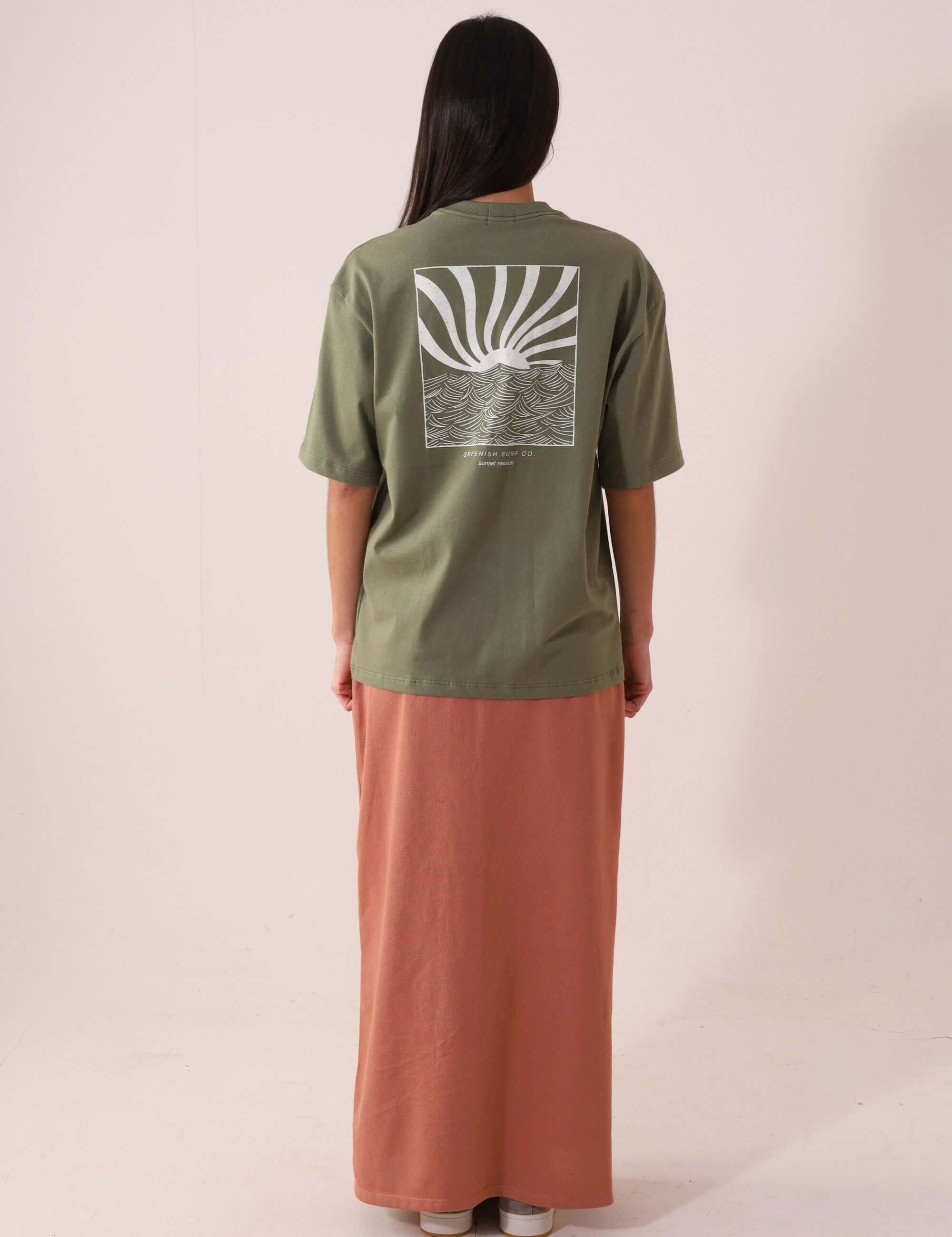 Mulher vestindo CAMISETA OVERSIZED SUNSET SESSION - VERDE Greenish com estampa de ondas e pôr do sol, vista traseira, estilo e conforto.