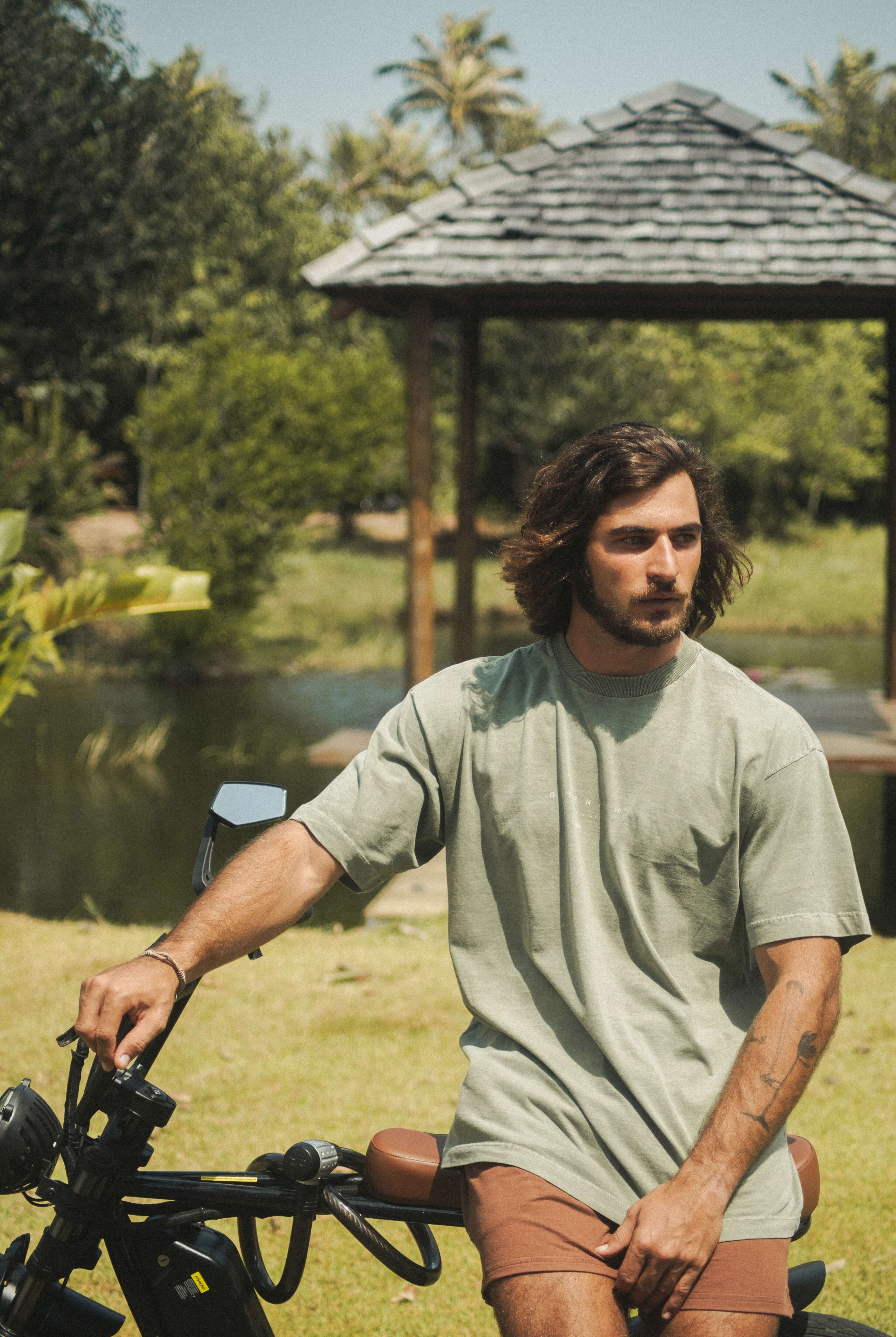Homem vestindo Camiseta Stone Oversized Greenish - Verde, da marca Greenish, sentado em uma bicicleta ao ar livre.