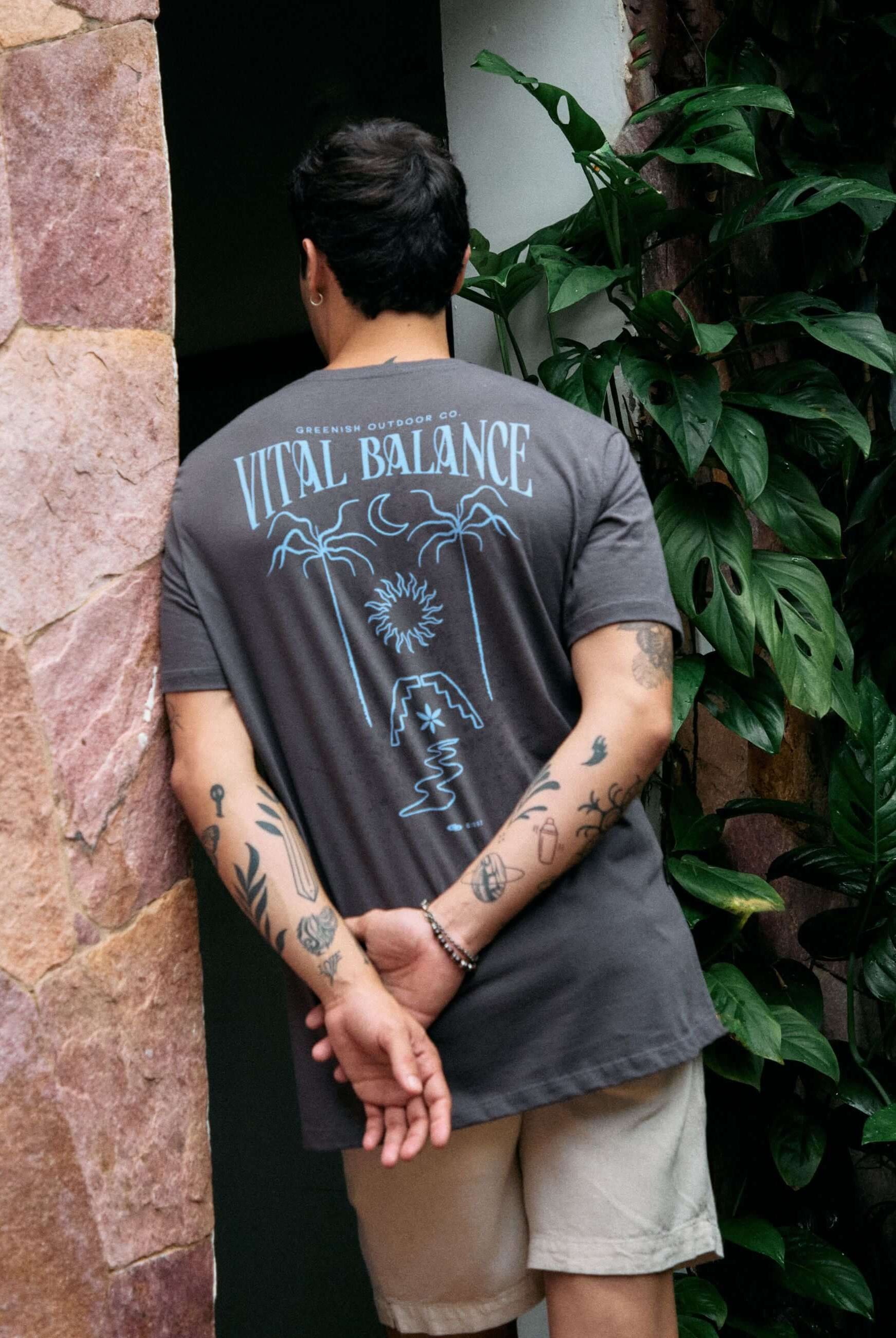 Alt Tag: Homem vestindo camiseta Grafite 'The Seed, The Sun and Moon' da Greenish com estampa de equilíbrio natural em um jardim.