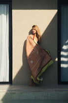 Mulher com Canga Vital Mood - Caqui da Greenish, destacando símbolos naturais em cores terrosas iluminadas pelo sol.