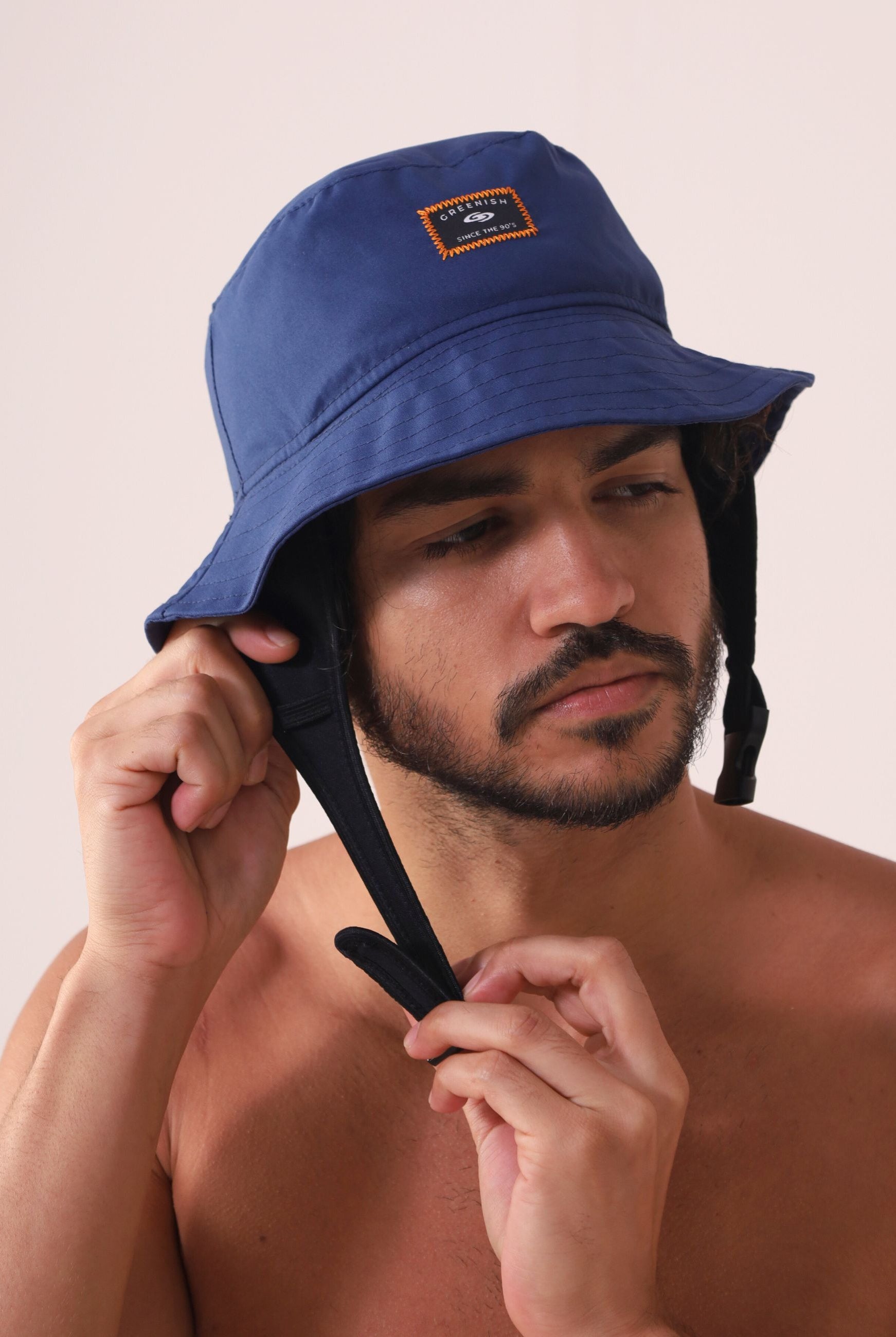 Homem ajustando Chapeu Bucket Sport - Azul Marinho da Greenish para atividades ao ar livre.