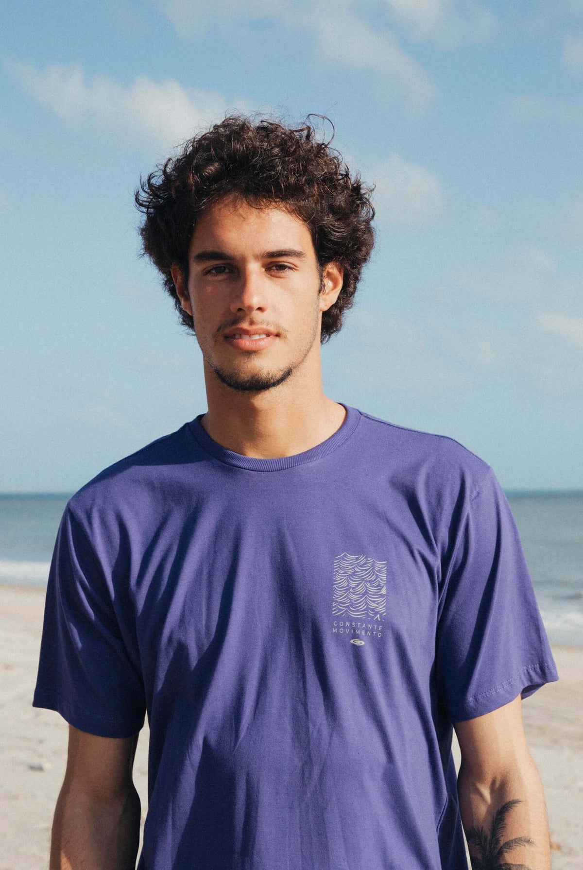 Camiseta Constantemente Movimento azul royal da Greenish, modelo masculino em frente ao mar.