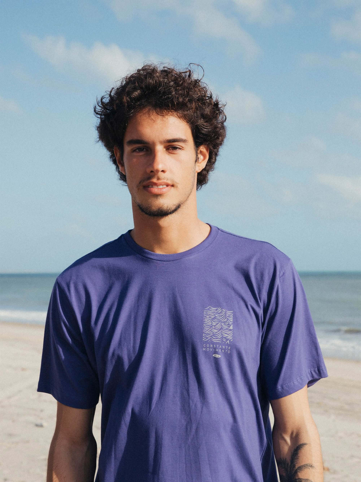 Camiseta Constantemente Movimento azul royal da Greenish, modelo masculino em frente ao mar.