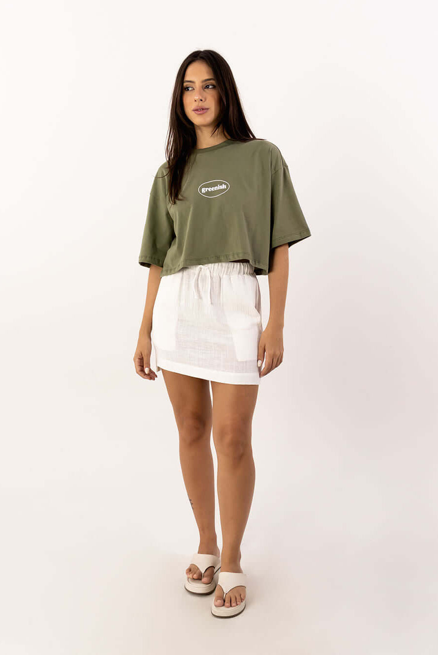 Modelo usando cropped oversized verde da Greenish com saia branca, look moderno e confortável.