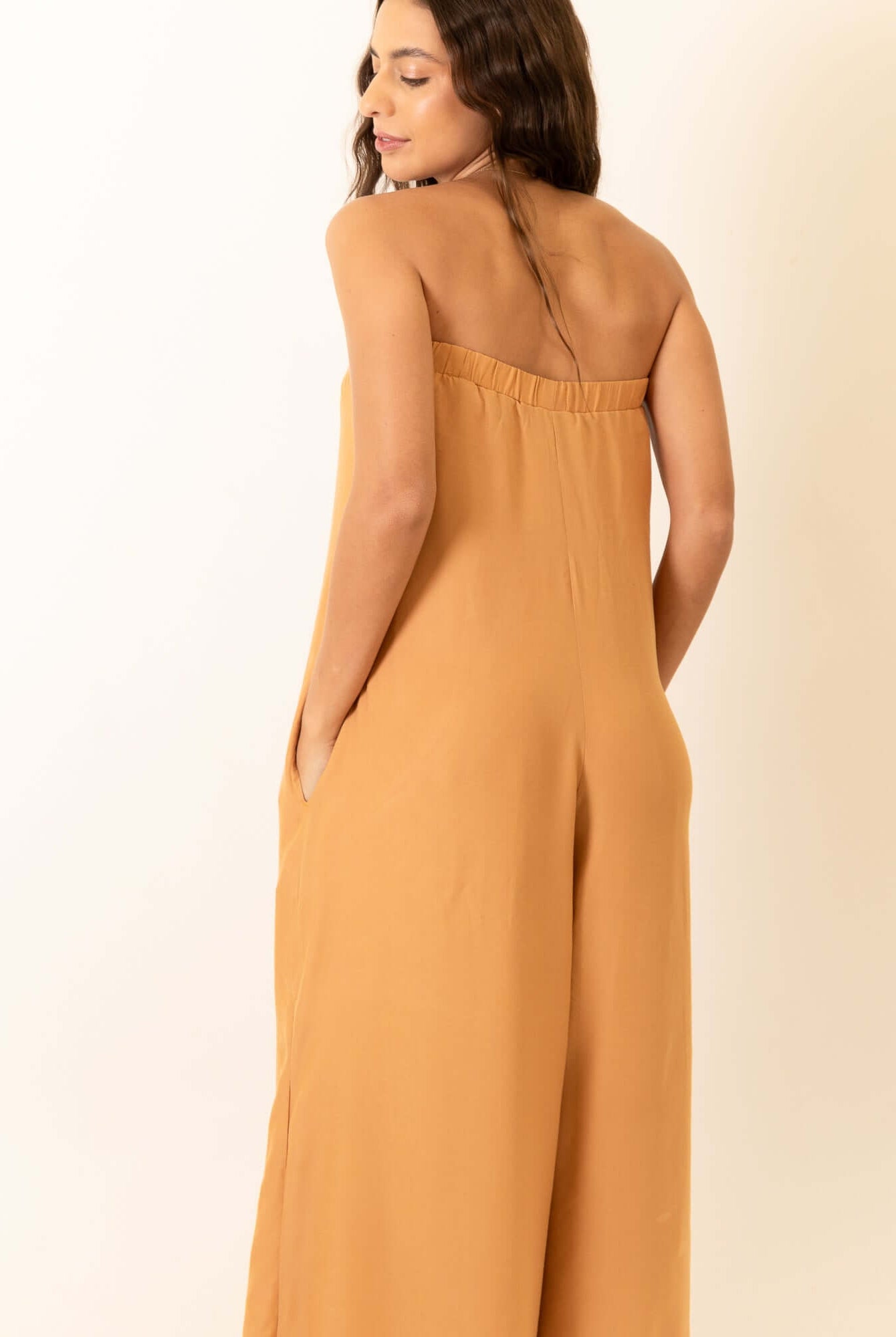 Modelo usando Macacão Leslie - Caqui por Greenish, visto por trás, destacando estilo e conforto.