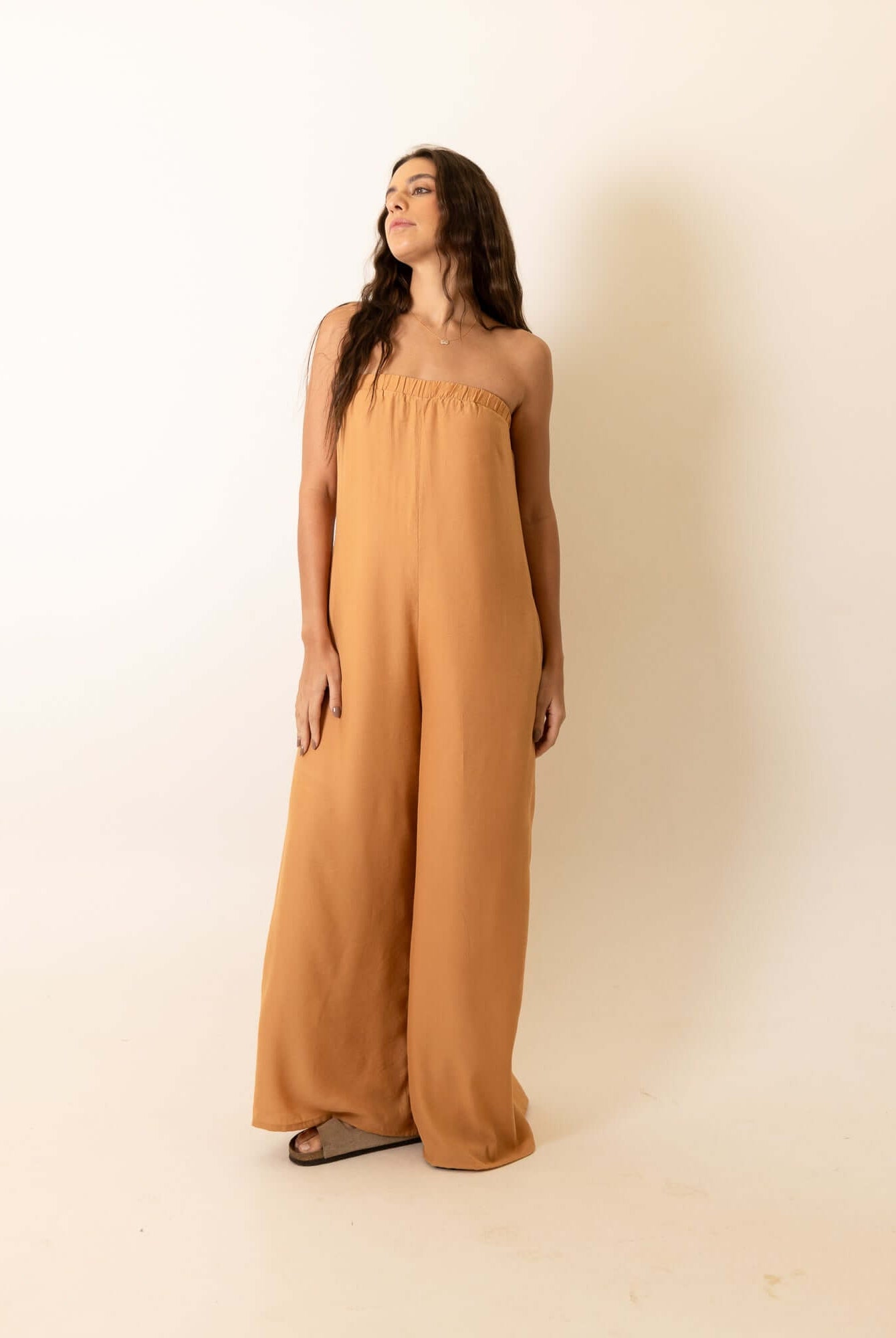 Mulher vestindo Macacão Leslie - Caqui da marca Greenish, destacando elegância e conforto. Peça chave para seu guarda-roupa.