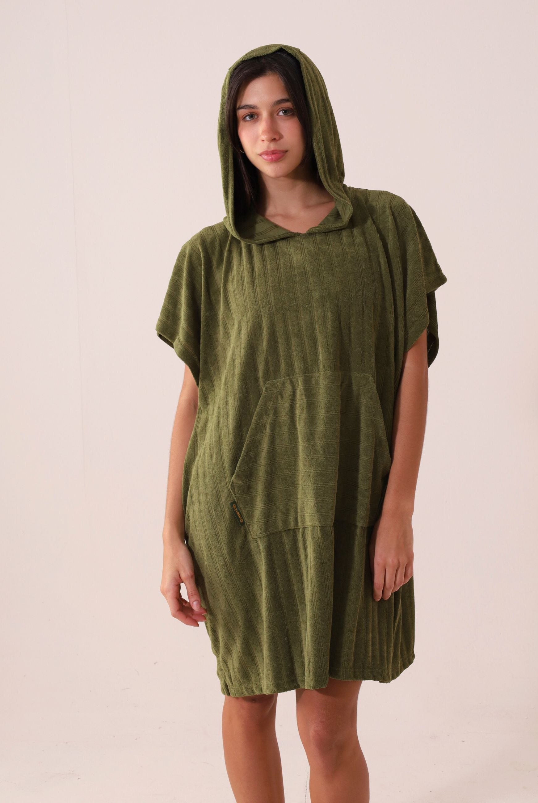 Mulher vestindo PONCHO CURTO CANELADO - VERDE da marca Greenish com capuz e bolso canguru, ideal para frio e esportes aquáticos.