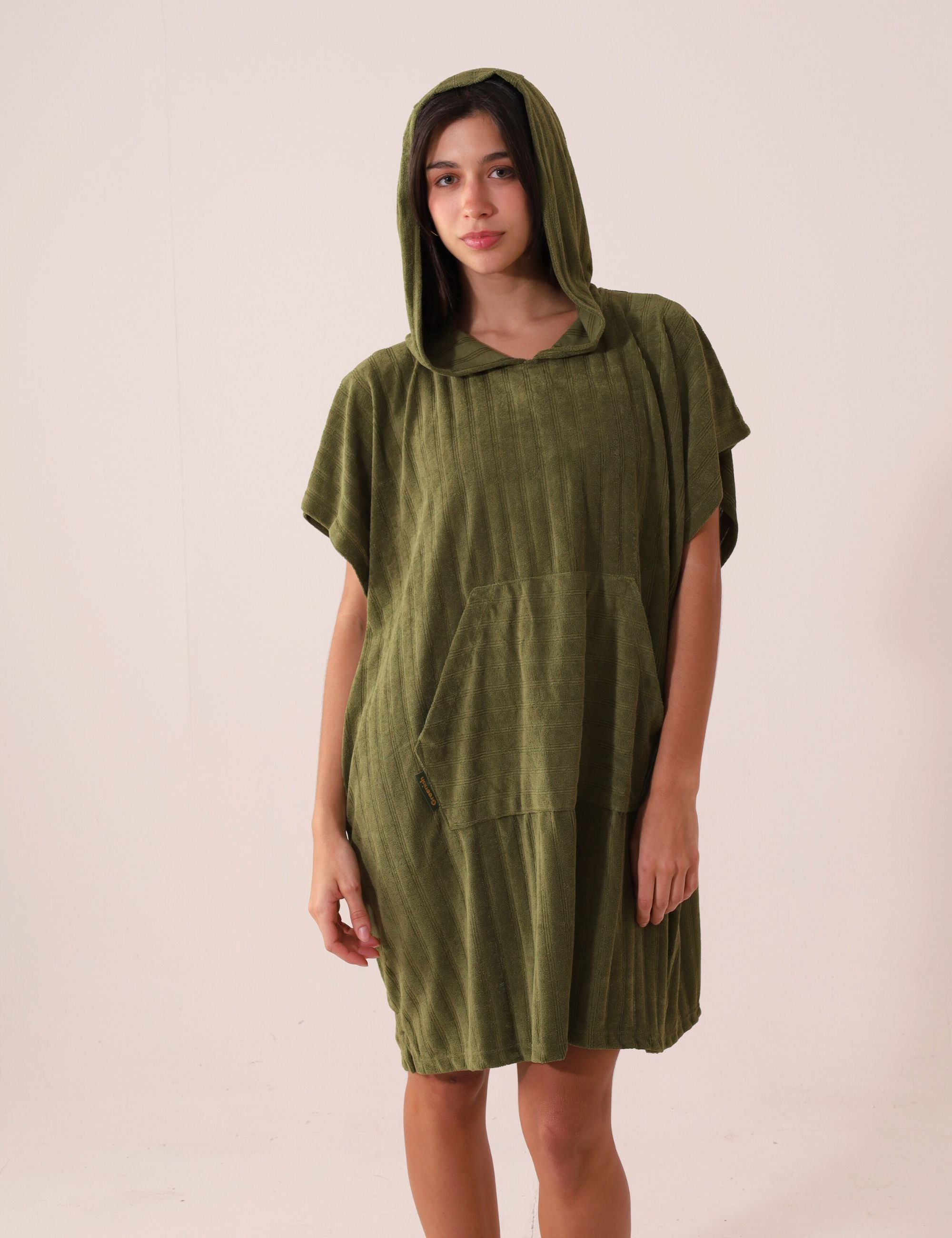 Mulher vestindo PONCHO CURTO CANELADO - VERDE da marca Greenish com capuz e bolso canguru, ideal para frio e esportes aquáticos.