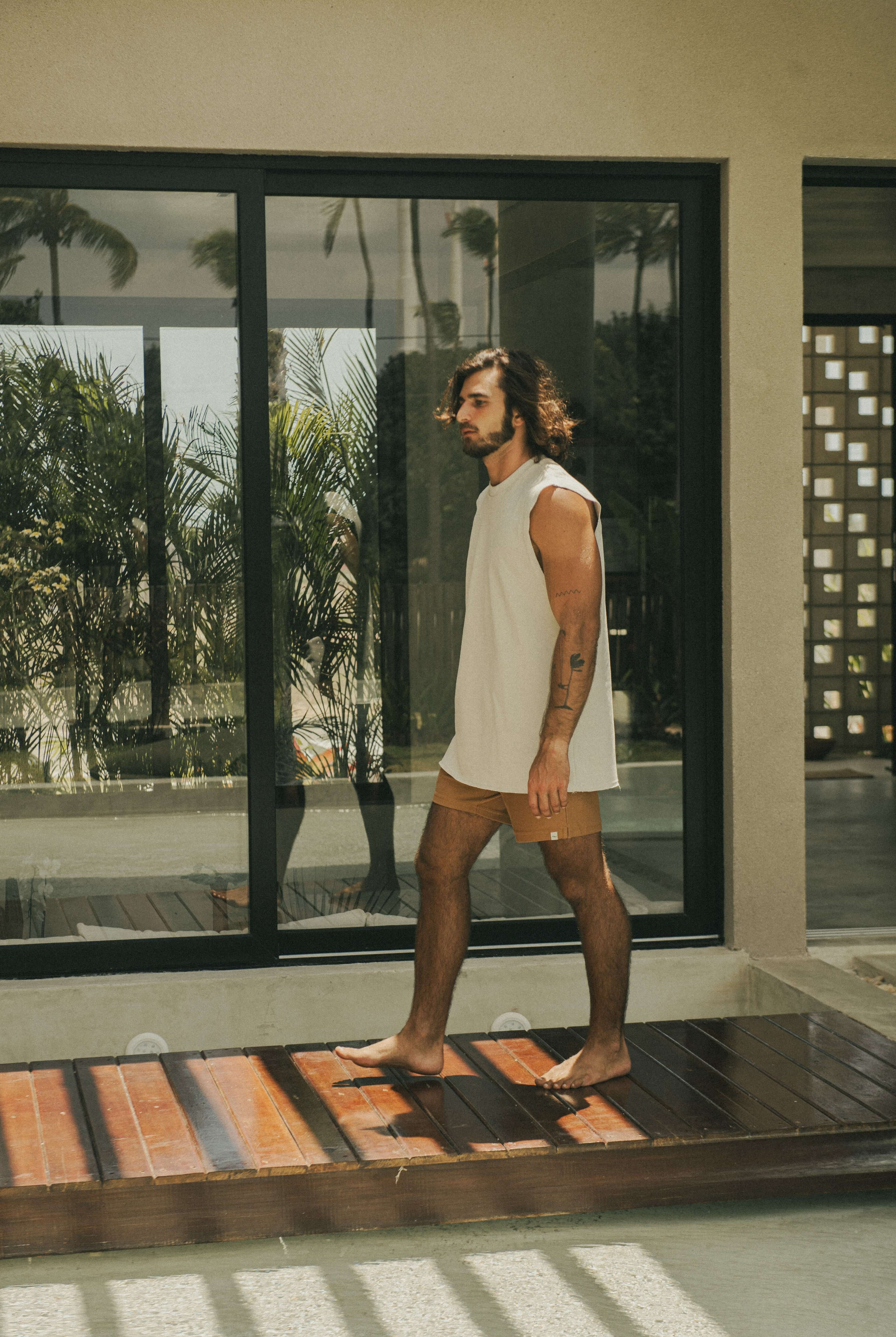 Homem usando Regata Larga Waves - Bege da marca Greenish em uma varanda ensolarada.