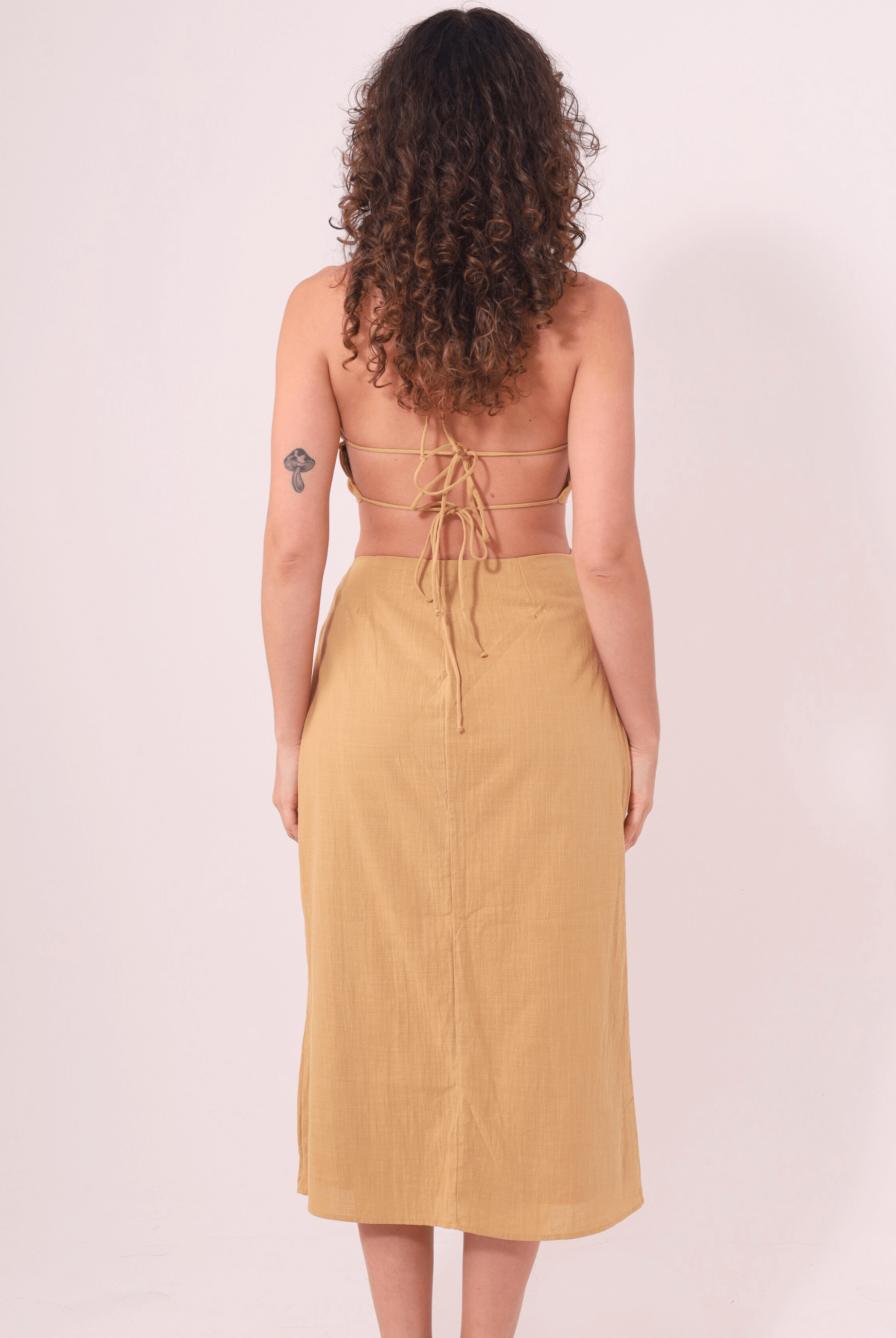 Mulher vestindo Saia Midi Sunny Caqui da Greenish, de costas, destacando o ajuste na cintura e tecido leve para dias de sol.