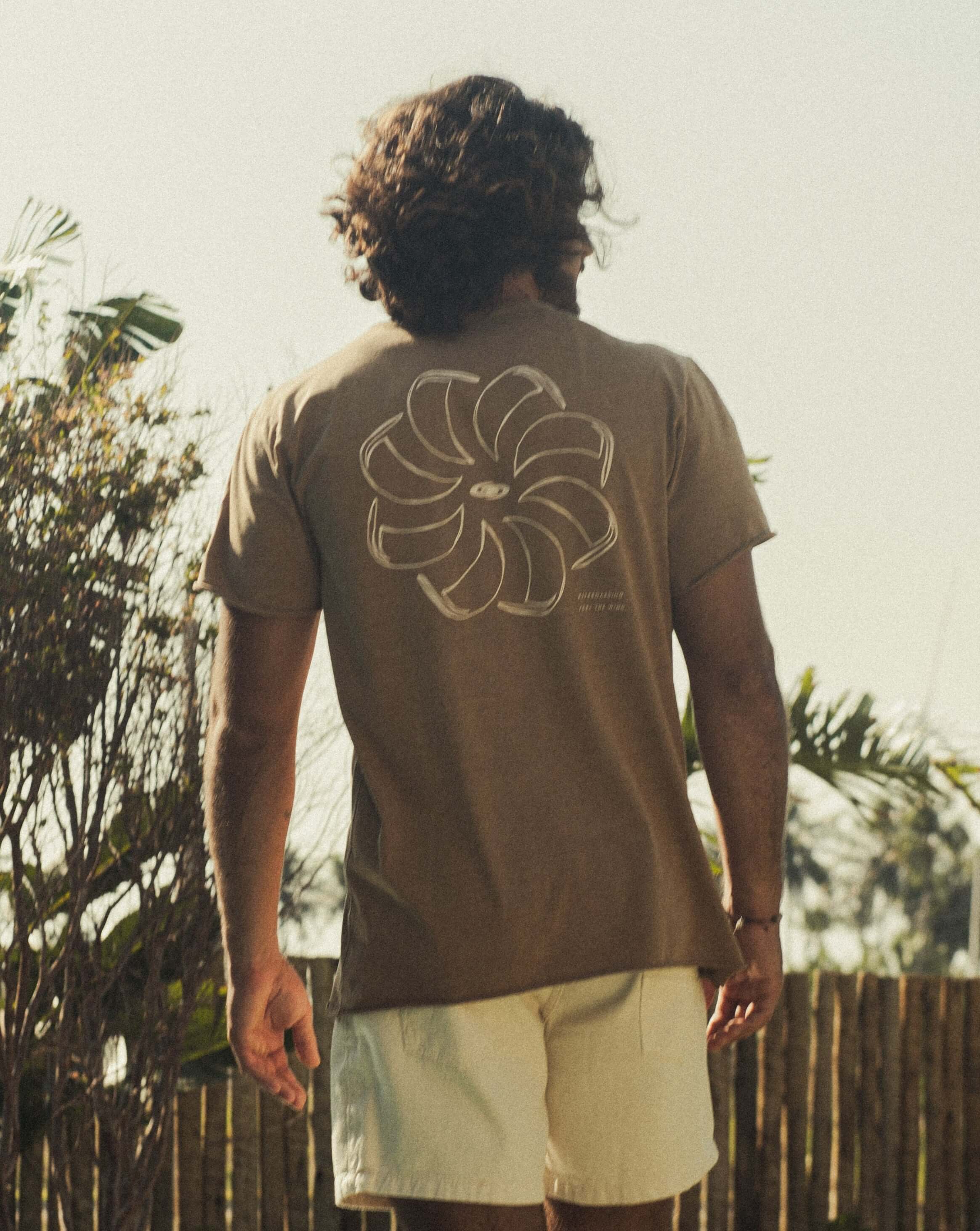 Camiseta Stone Feel The Winds - Marrom da Greenish, modelo básico em meia malha 100% algodão, vista de costas em ambiente natural.