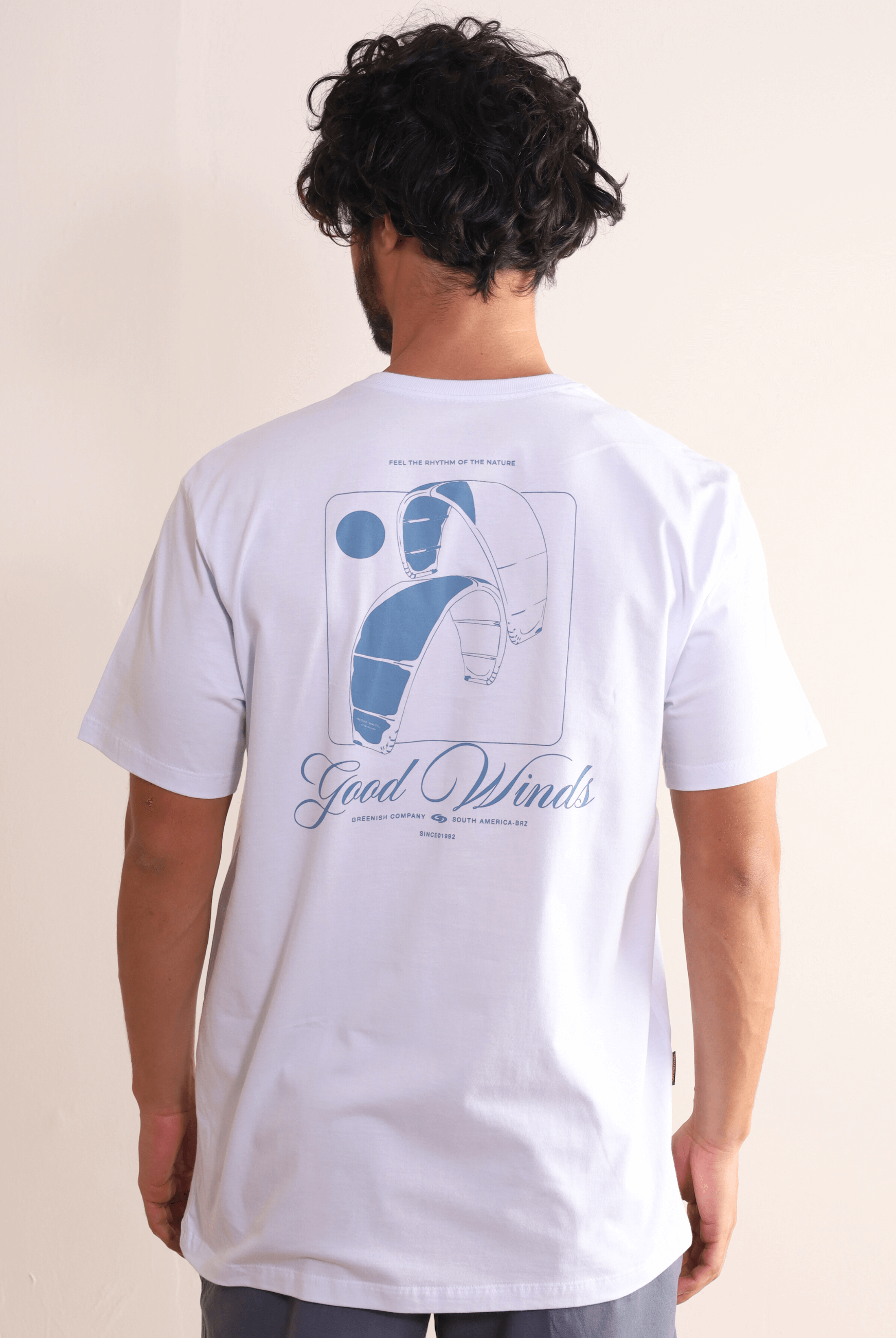 Homem vestindo camiseta Greenish Kites & Good Winds branca com arte de kite nas costas.