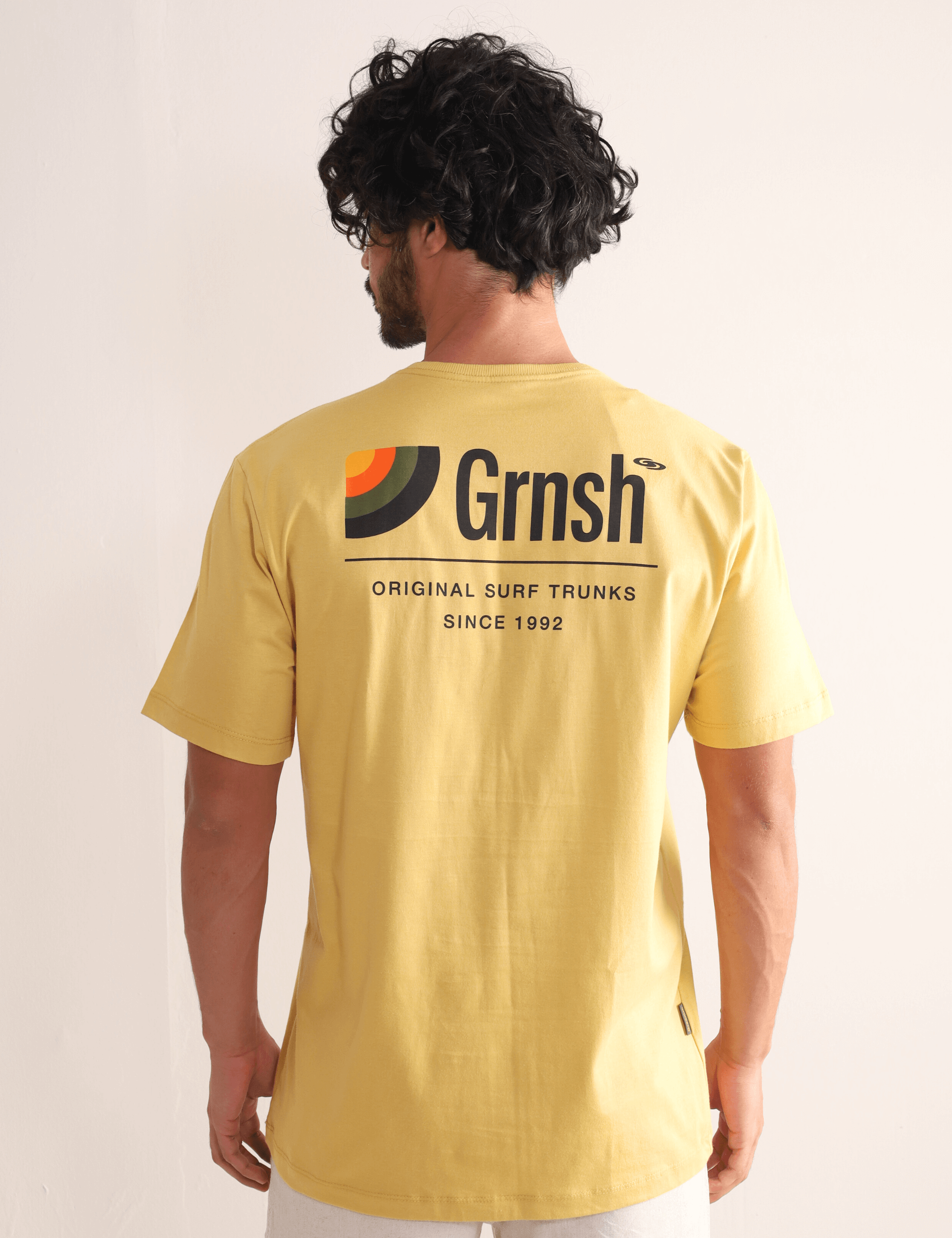 Modelo vestindo camiseta Greenish Original Surf Trunks Serie I em amarelo escuro, com estampa inspirada no lifestyle litorâneo.