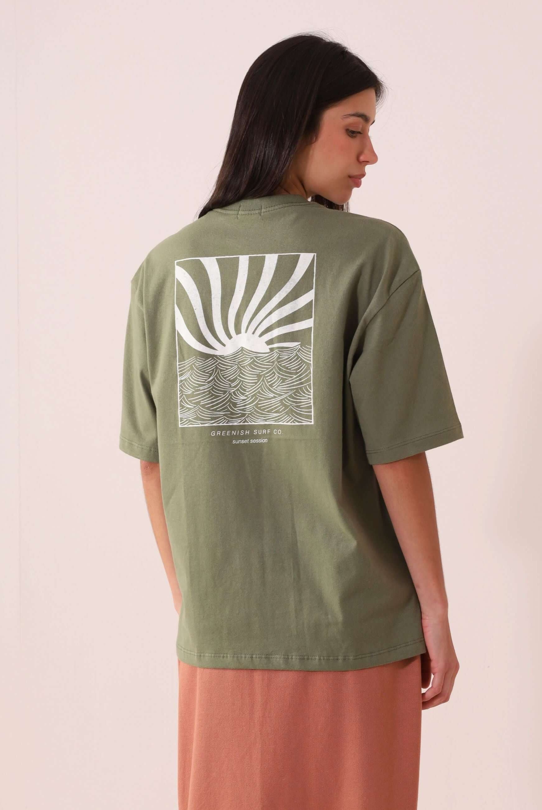 Modelo usando CAMISETA OVERSIZED SUNSET SESSION - VERDE da Greenish com estampa de ondas e pôr do sol nas costas, estilo e conforto.
