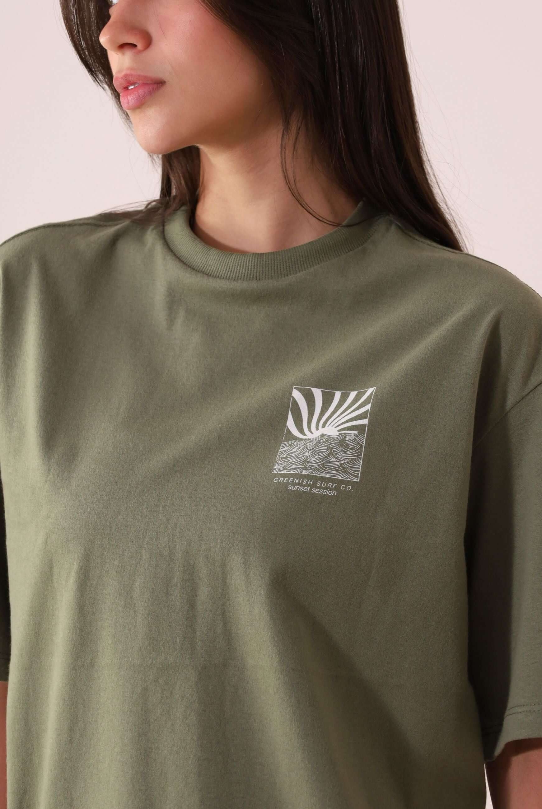 Mulher vestindo CAMISETA OVERSIZED SUNSET SESSION - VERDE da Greenish, com estampa de ondas ao pôr do sol, em tecido 100% algodão.