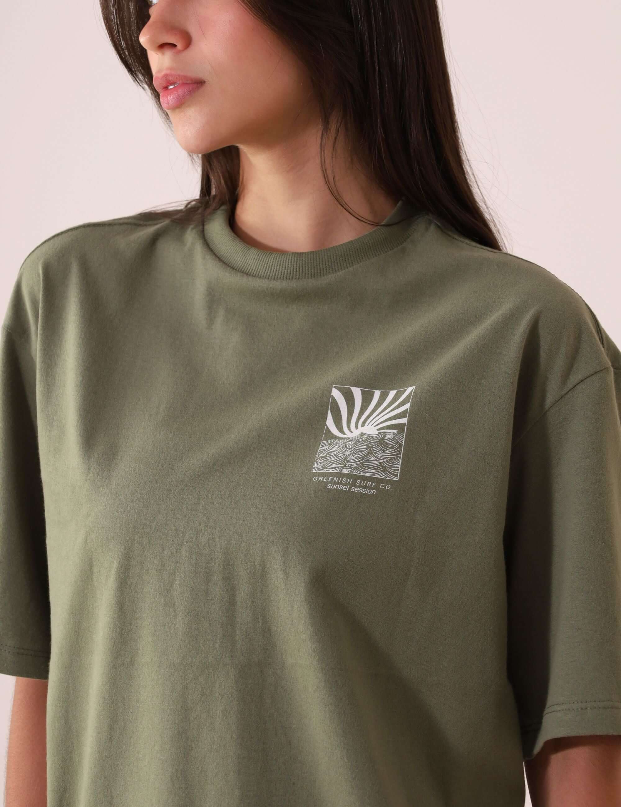 Mulher vestindo CAMISETA OVERSIZED SUNSET SESSION - VERDE da Greenish, com estampa de ondas ao pôr do sol, em tecido 100% algodão.