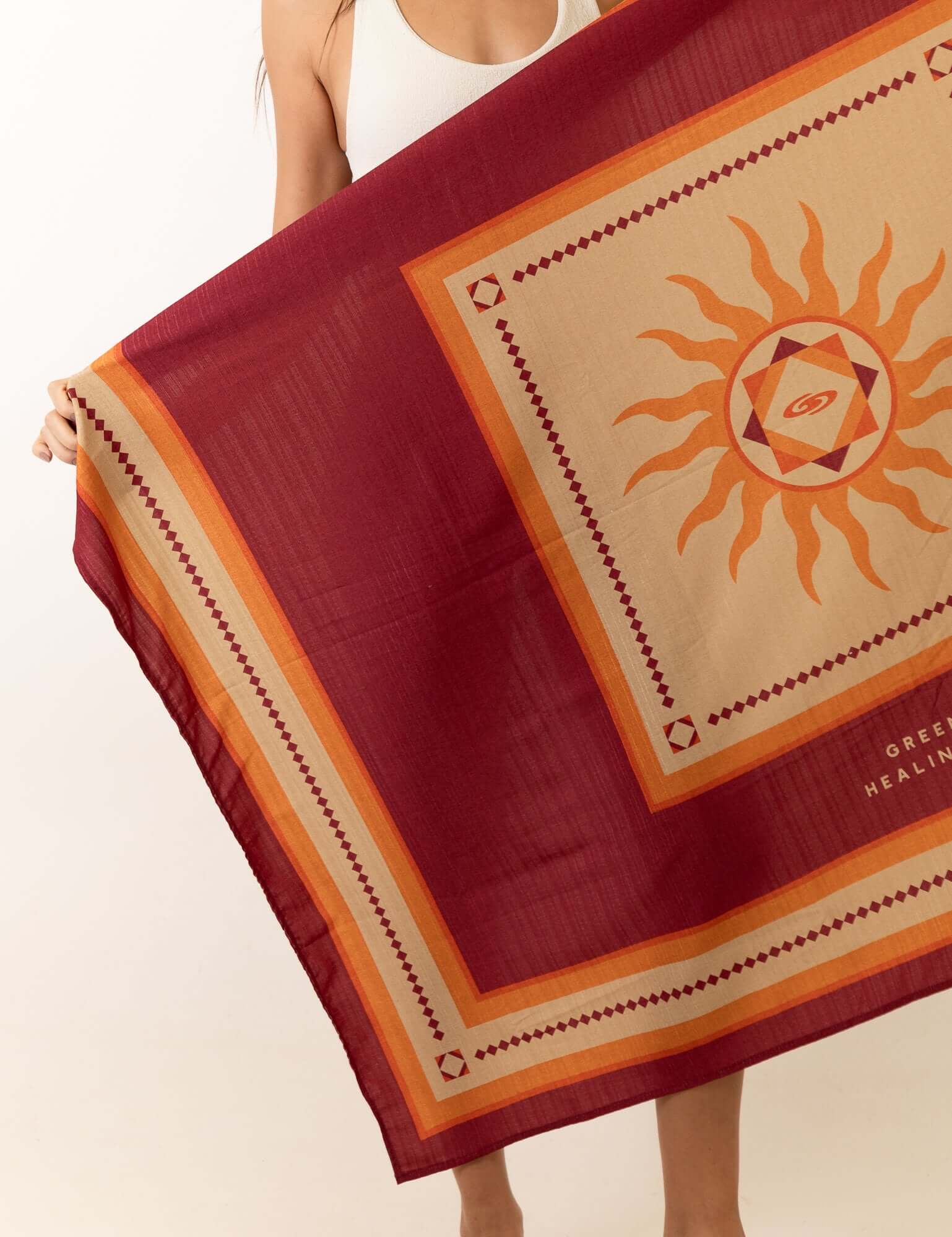 Mulher segurando a Canga Healing Rays - Bordo da Greenish, com estampa solar e estética vintage bordô.