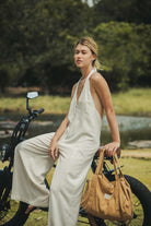 Mulher vestindo Macacão Longo Gaia - Natural da Greenish, em linho leve, ao lado de uma bicicleta, destacando estilo e conforto.