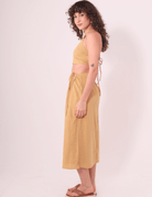 Modelo usando Saia Midi Sunny Caqui da Greenish, algodão 100%, com amarração ajustável para conforto e fluidez em dias ensolarados.