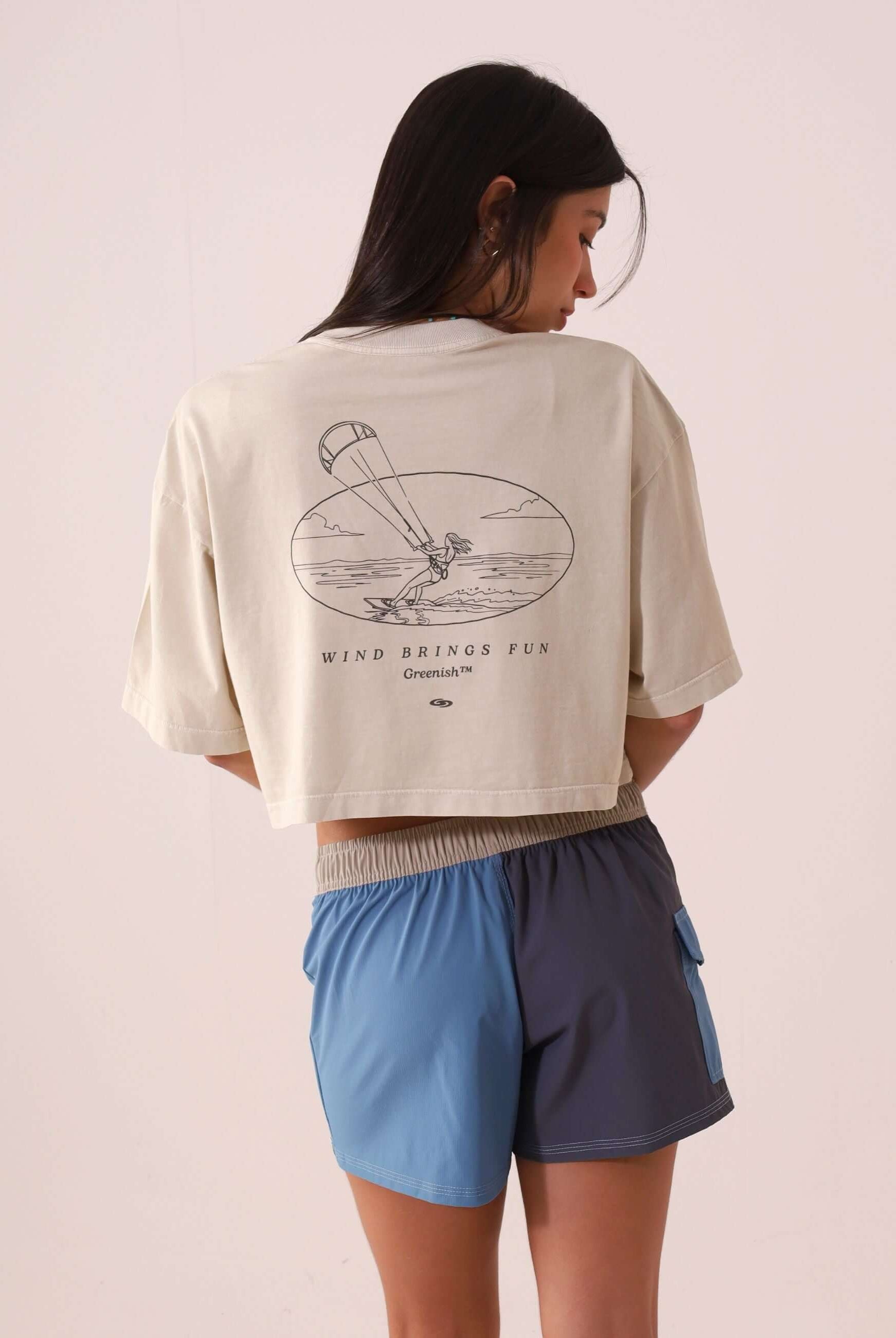 Mulher vestindo SHORT SPORT TALITA - AZUL da marca Greenish, visto de costas com camiseta curta e estampa de vento e diversão.