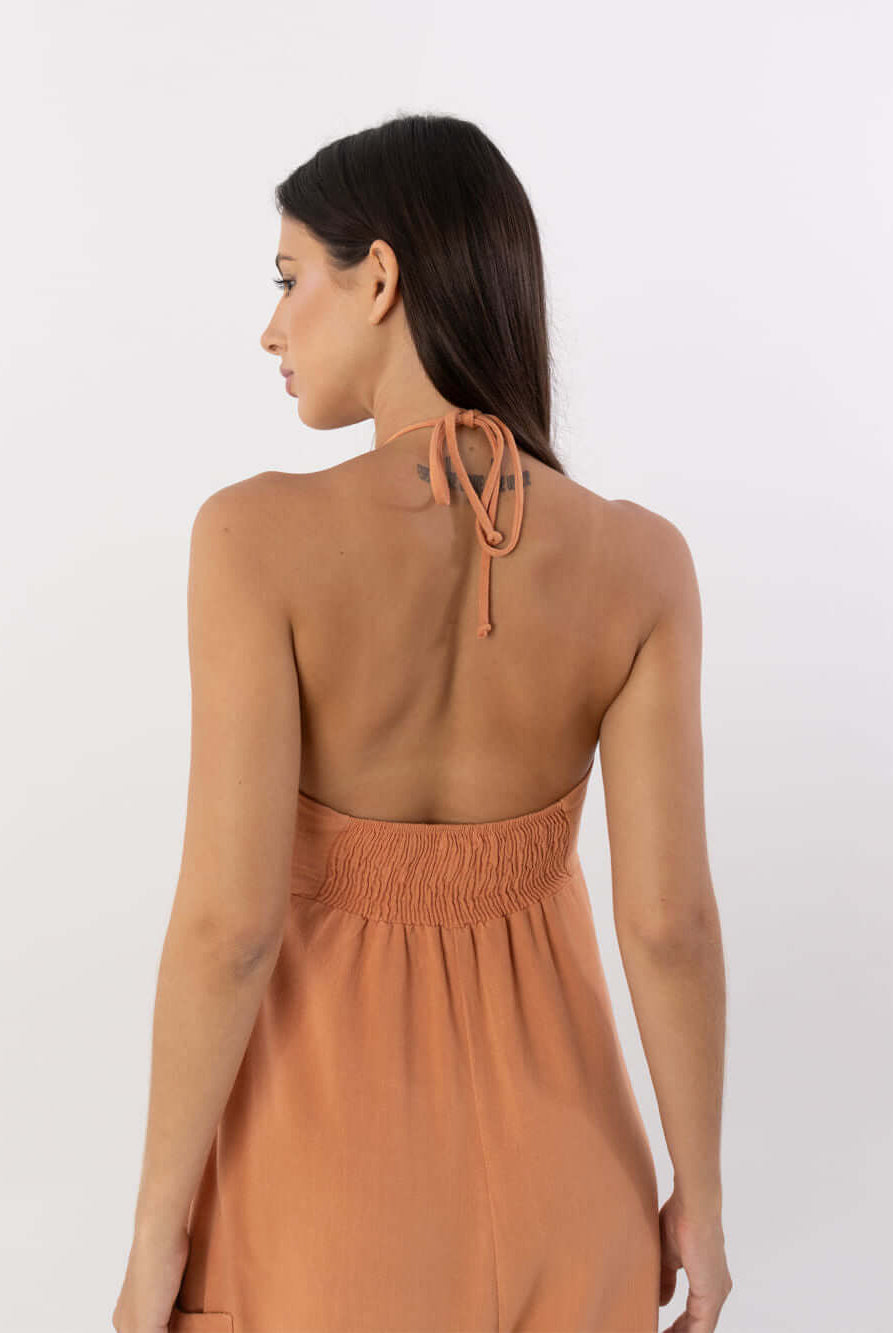 Mulher de costas vestindo macacão coral Ana da marca Greenish, mostrando detalhe do laço no pescoço.