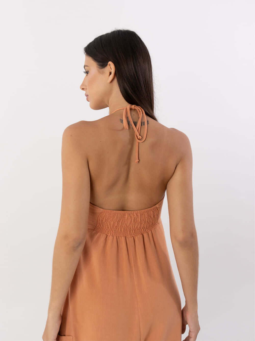 Mulher de costas vestindo macacão coral Ana da marca Greenish, mostrando detalhe do laço no pescoço.