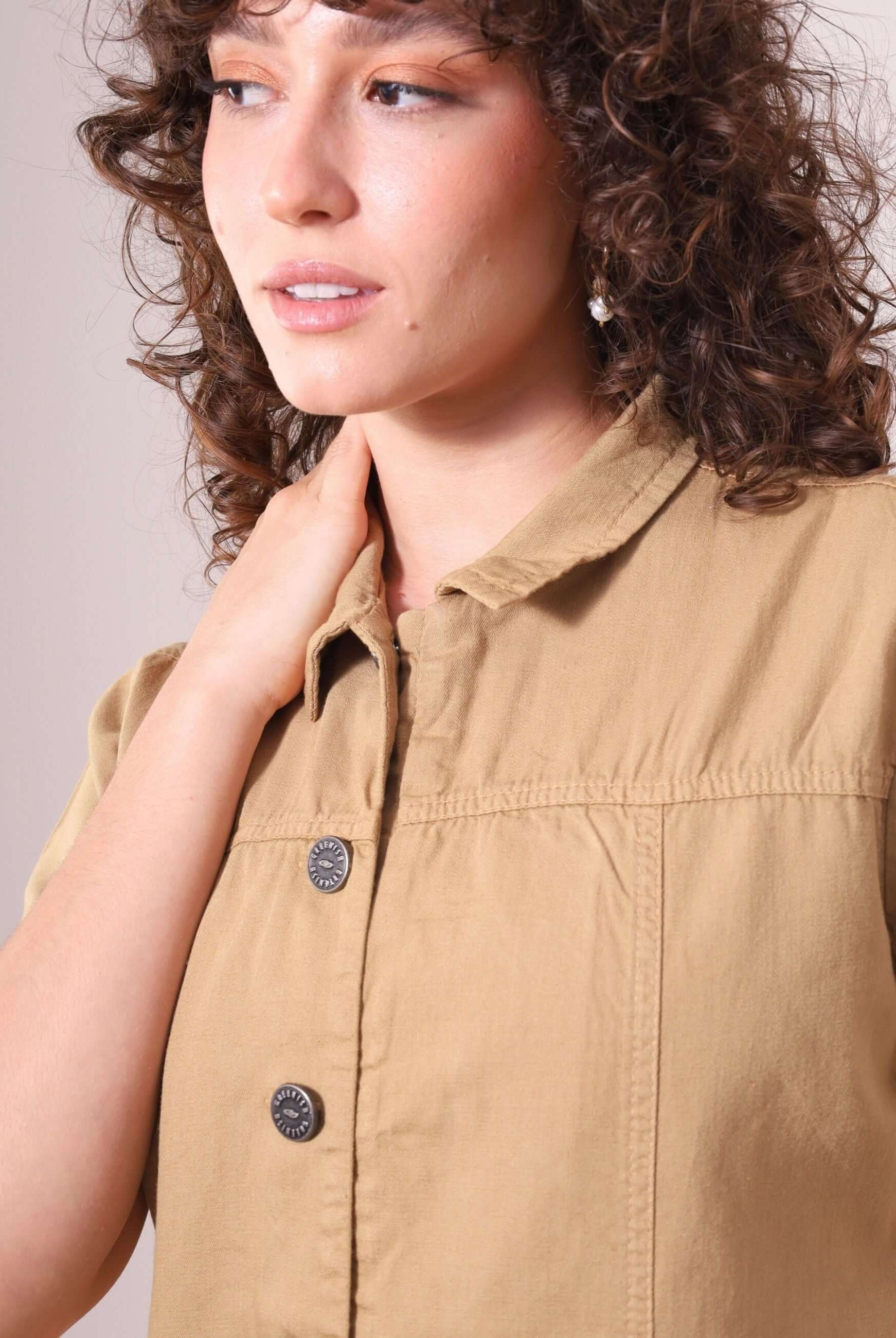 Mulher vestindo o Macacão Ivy Bege da Greenish, destacando gola estruturada e botões frontais. Estilo utilitário e conforto em sarja 100% algodão.
