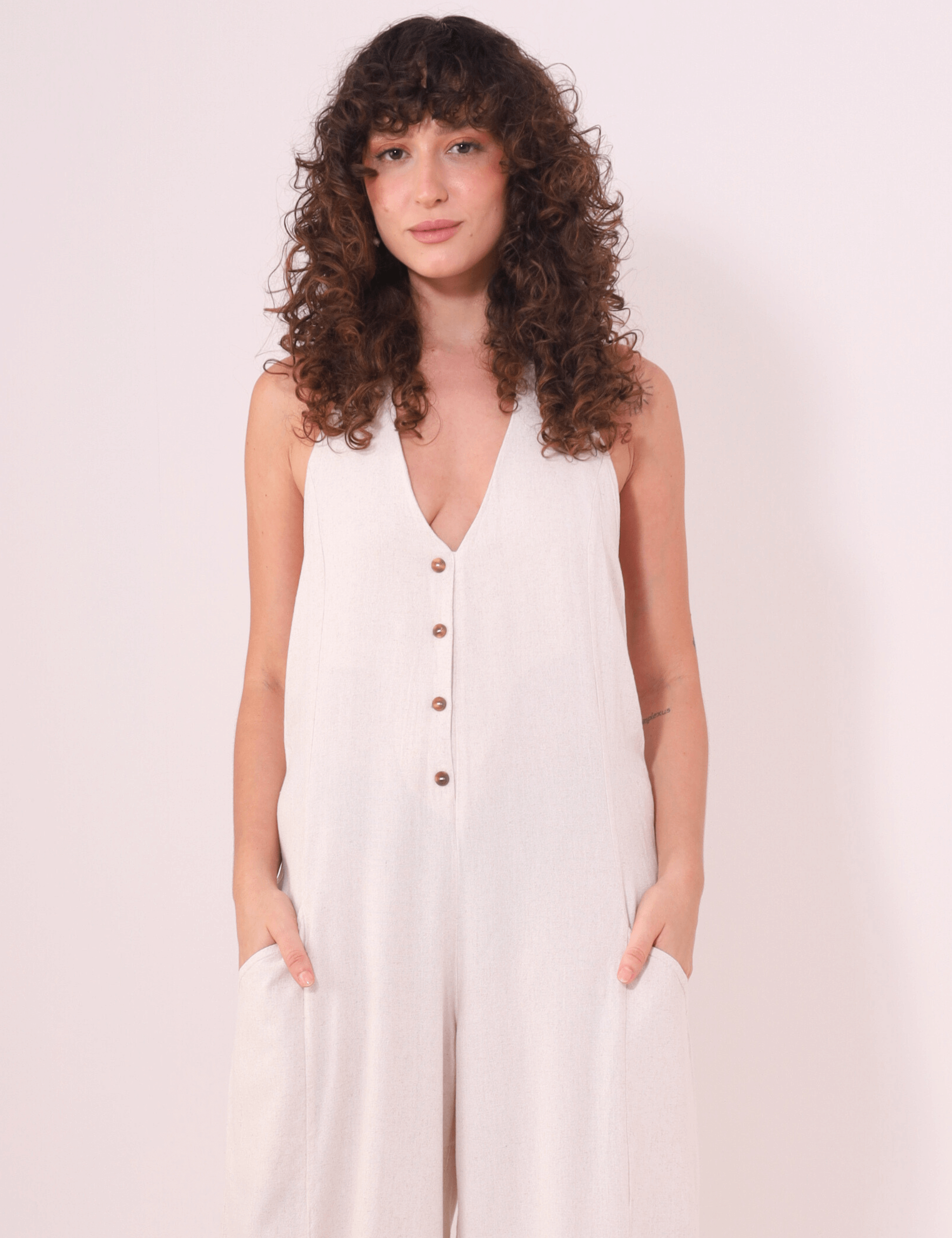 Modelo vestindo Macacão Longo Gaia - Natural da Greenish, feito de linho leve com decote halter e botões decorativos.