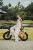 Mulher usando o Macacão Longo Gaia - Natural da Greenish, tecido de linho leve e fresco, em ambiente natural ao lado de uma bicicleta elétrica.