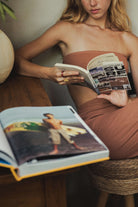 Mulher lendo livro vestindo o Macacão Longo Riviera - Cacau da Greenish, destacando design elegante e silhueta sofisticada.