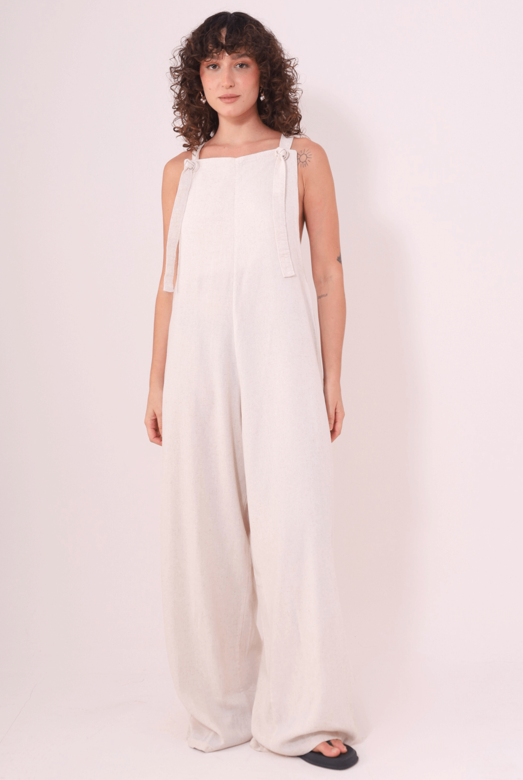 Mulher vestindo Macacão Khay - Natural de Linho Washed Soft da marca Greenish, com costas nadador e modelagem confortável para dias quentes.