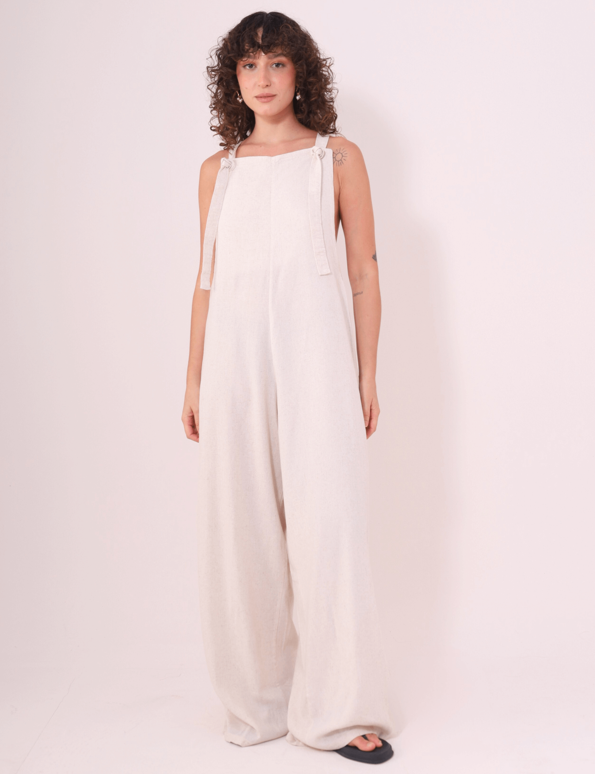 Mulher vestindo Macacão Khay - Natural de Linho Washed Soft da marca Greenish, com costas nadador e modelagem confortável para dias quentes.