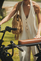 Mulher vestindo Macacão Longo Gaia - Natural da Greenish, com design leve e fluido, ao lado de bicicleta em ambiente externo.