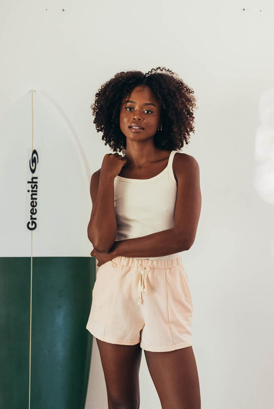 Moletom Clay laranja da Greenish, modelo solto e confortável, perfeito para o dia a dia, com a surfista ao fundo.