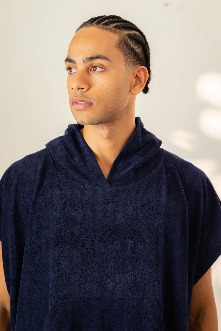 Homem usando poncho adulto azul marinho da Greenish, ideal para praia e esportes aquáticos.