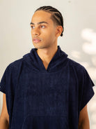 Homem usando poncho adulto azul marinho da Greenish, ideal para praia e esportes aquáticos.