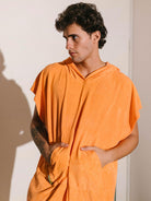 Homem usando poncho adulto cor laranja da Greenish, com bolsos canguru e tecido atoalhado.