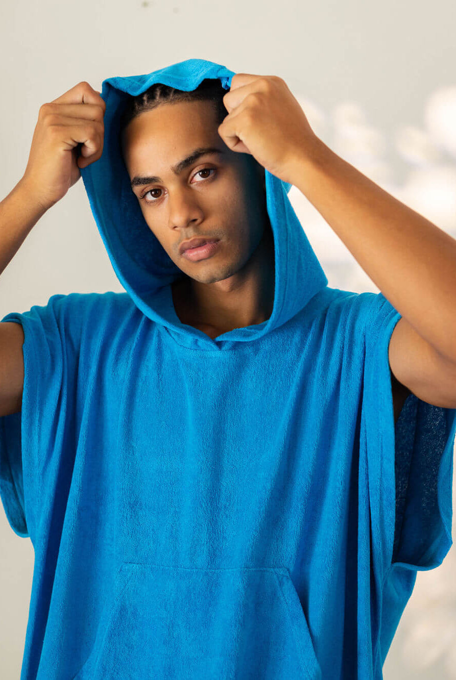 Jovem usando poncho adulto canguru turquesa da marca Greenish, perfeito para a praia e secagem rápida.