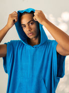 Jovem usando poncho adulto canguru turquesa da marca Greenish, perfeito para a praia e secagem rápida.