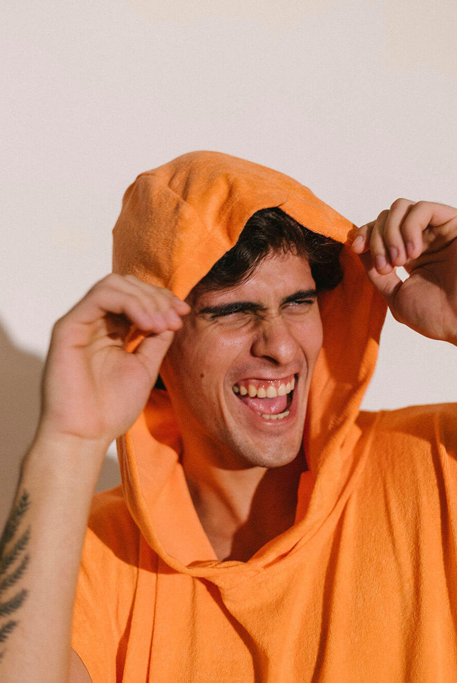 Homem sorrindo vestindo poncho adulto Greenish cor coral com capuz, destacando seu conforto e estilo.