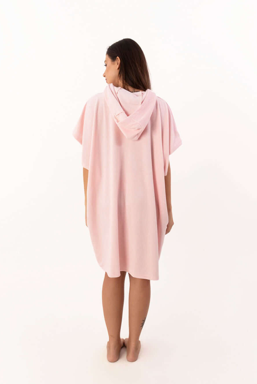 Modelo de poncho curto atoalhado rosa claro com capuz visto de costas, ideal para praia e esportes aquáticos.