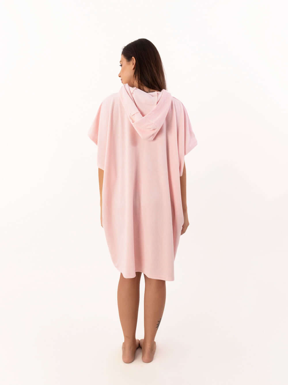 Modelo de poncho curto atoalhado rosa claro com capuz visto de costas, ideal para praia e esportes aquáticos.